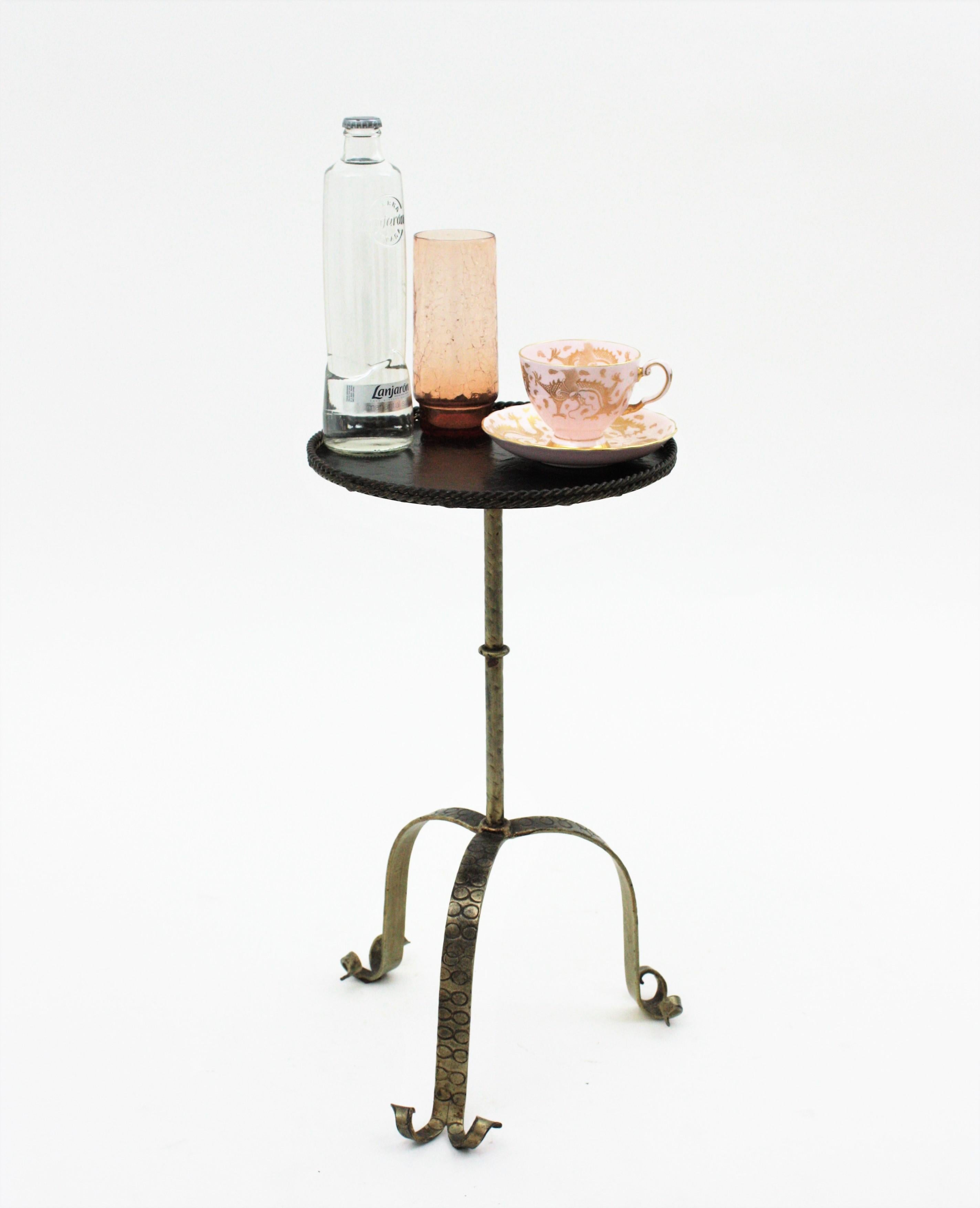 Hand forged iron Martini table, stand or drinks table, Spain, 1960s.
This nice end table has a black patinated top with an iron braided rope surrounding the edge. It stands on a gilt iron tripod base with scroll ended feet and hammered details