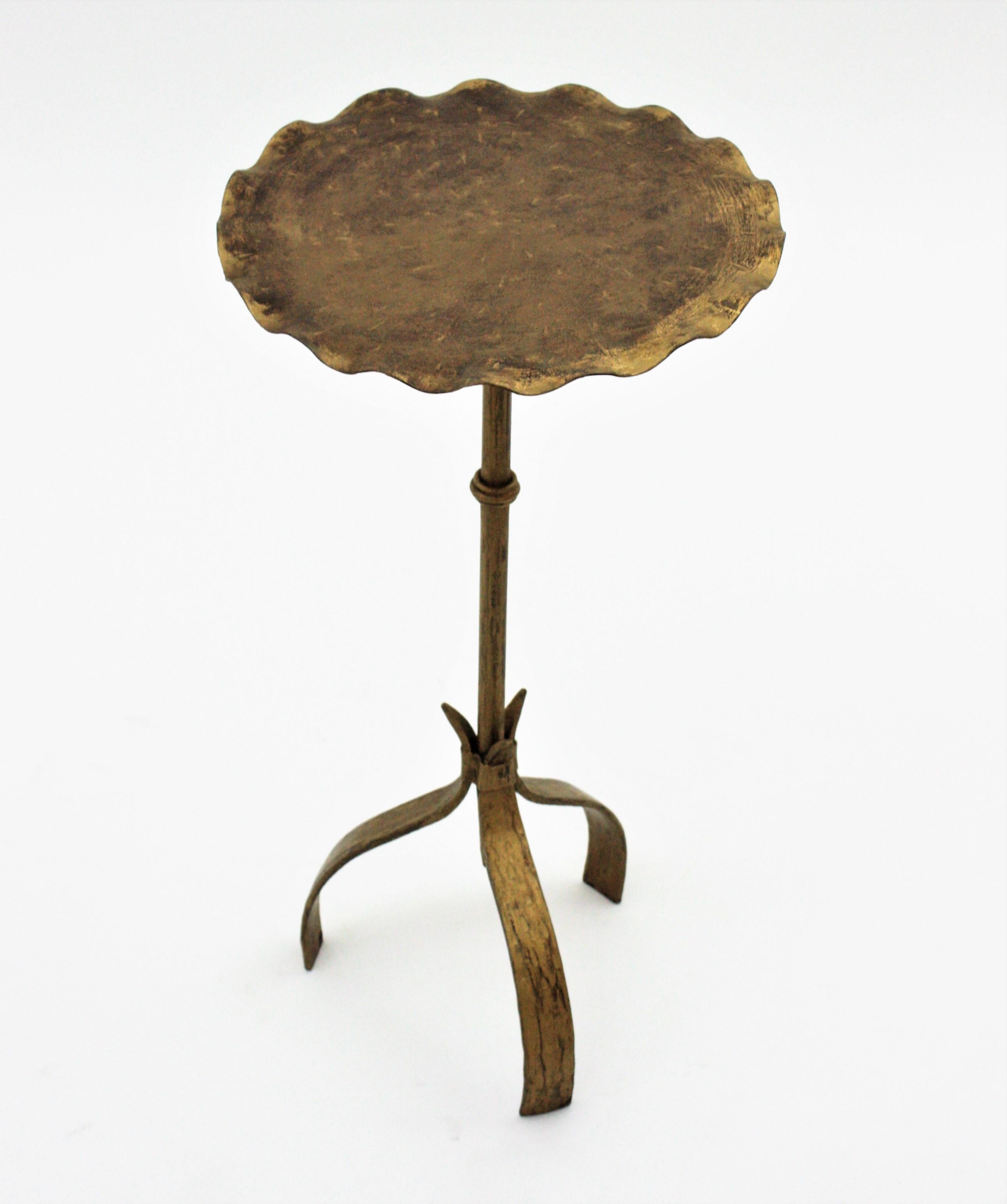 Spanish gilt wrough iron drinks table gueridon, end or side table. Manufactured in Spain, 1950s.
This pedestal table has a round top with wavy edge heavily decored by the hammer work. It stands on a tripod base with a ring detail at the stem .