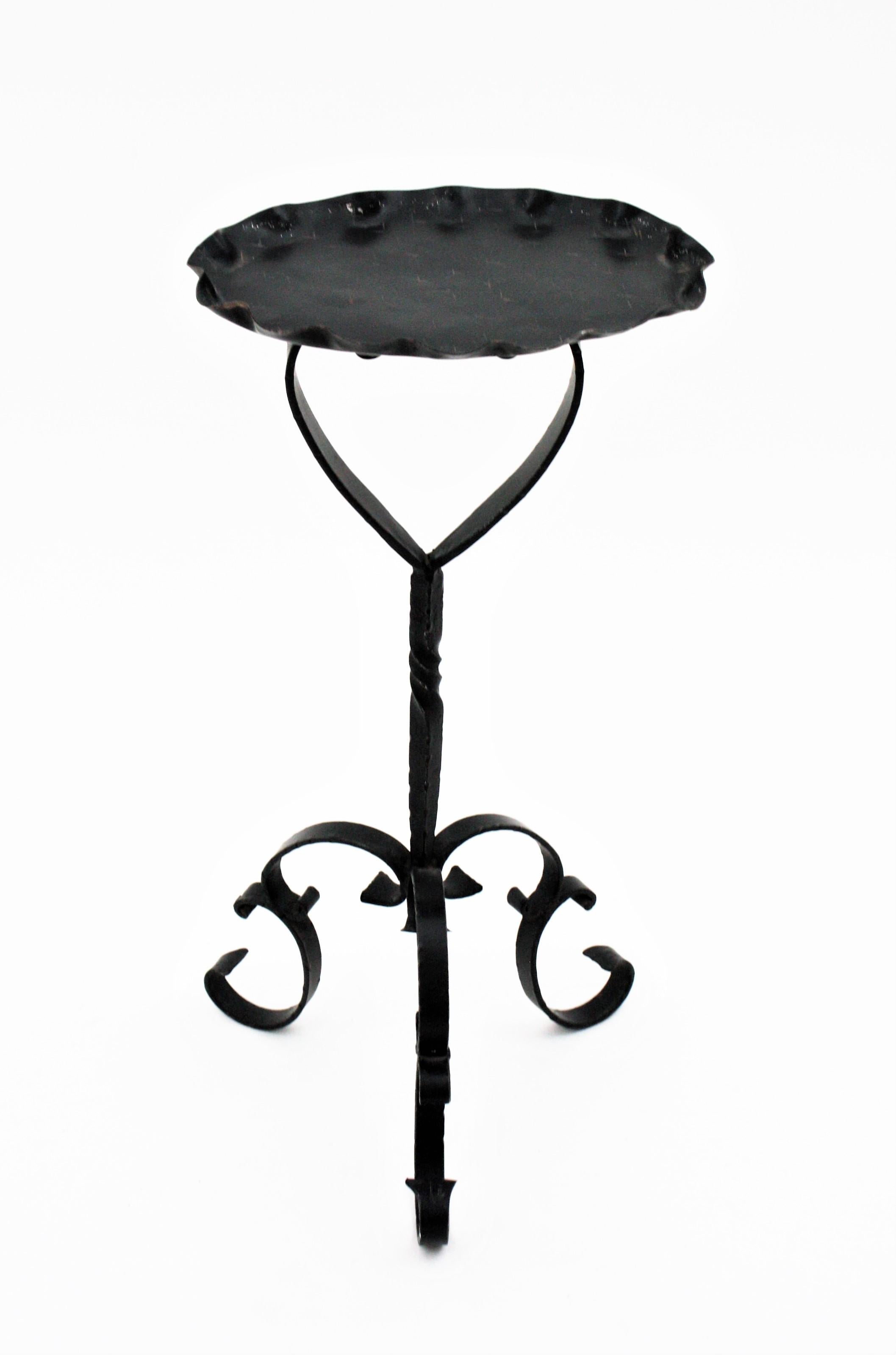 Spanish black wrough iron drinks table gueridon, end or side table. Manufactured in Spain, 1950s-1960s.
This pedestal table has an oval wavy edged top heavily decored by the hammer work. It stands on a tripod base with twisting details at the stem