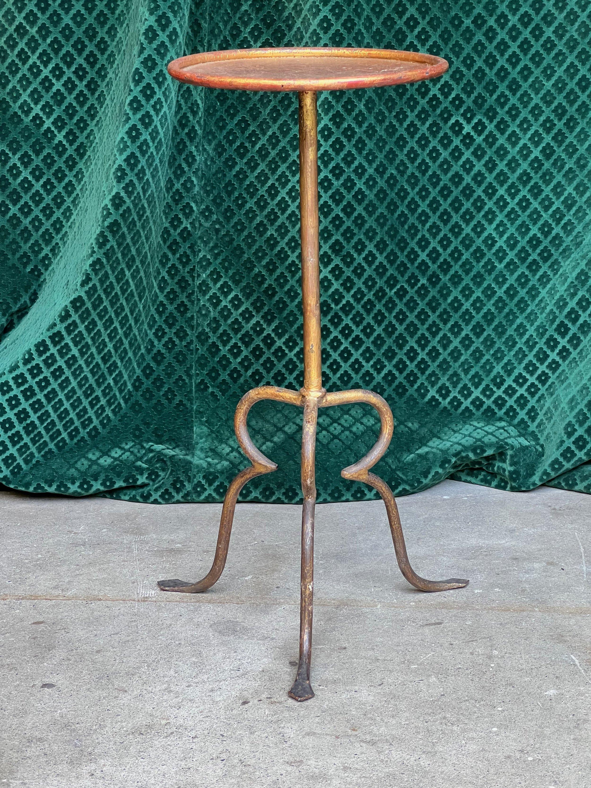 This unique drinks table, standing on a tripod base, offers an unusual yet aesthetically pleasing design. The table features an original hand-applied gold finish with darker undertones, resulting in a rich and distinctive look. The top surface,