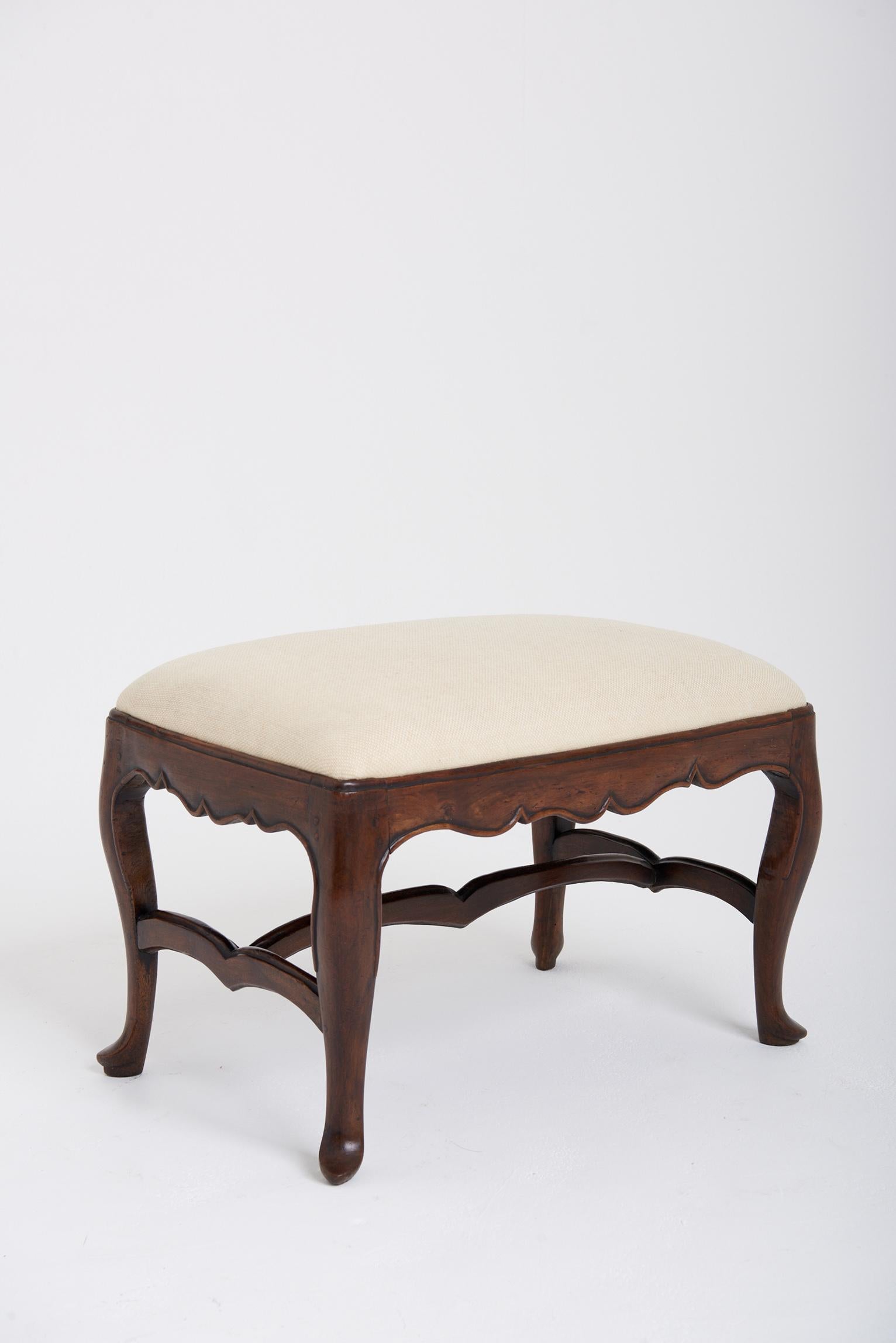 A carved walnut stool, the padded seat above a shaped frieze on cabriole legs joined by a shaped H-stretcher. 
Reupholstered in tweed.
Spain, first quarter of the 18th century.