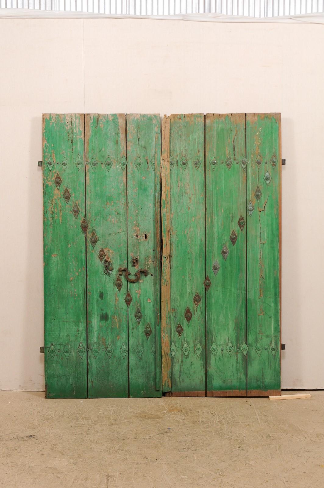 A pair of Spanish carved wood doors from the early 19th century. This pair of antique doors from Spain each feature three vertically positioned boards with old green paint and a geometric pattern of forged iron hardware and diamond-shaped rivets