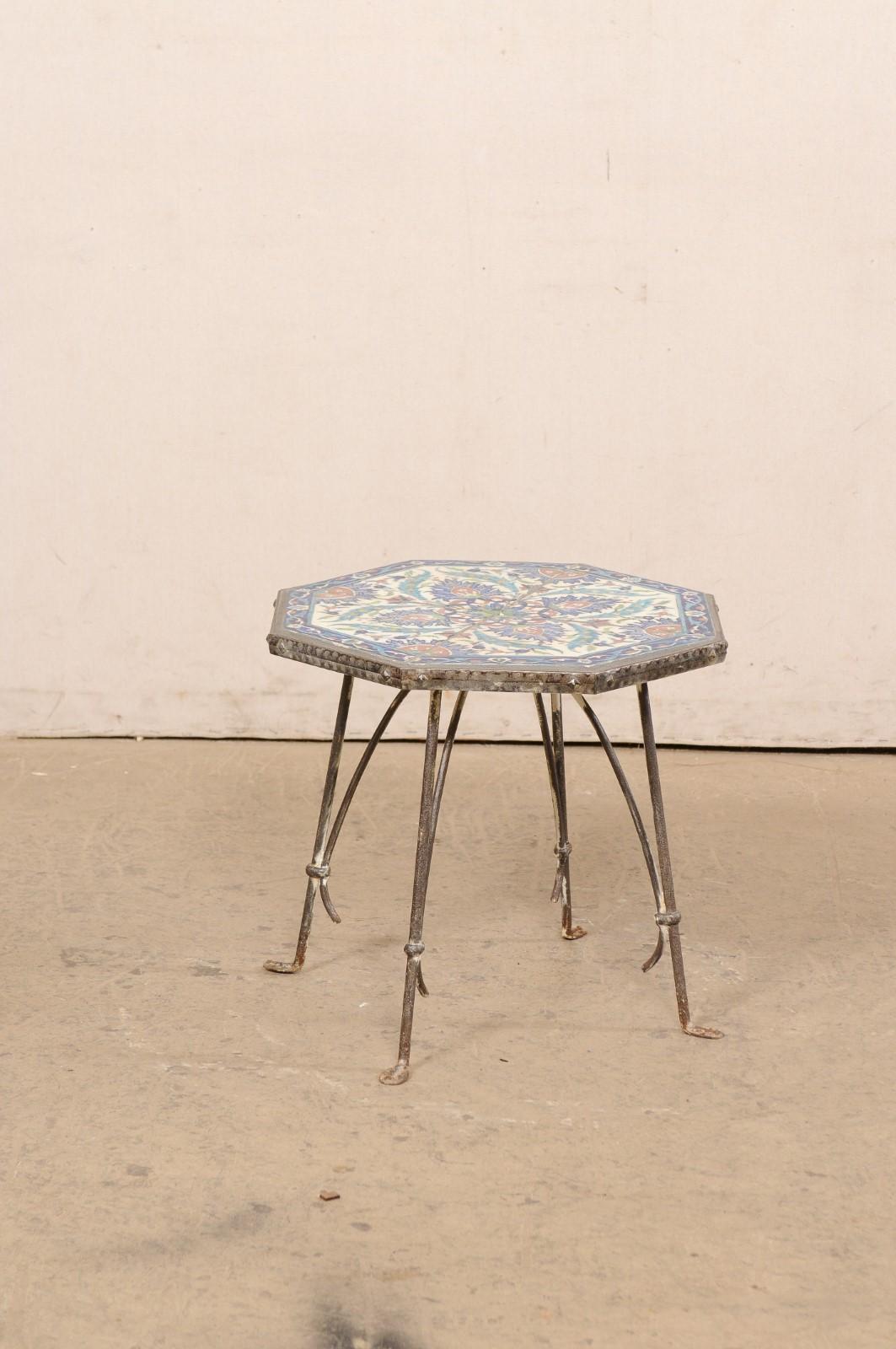 A Spanish iron accent table with tile top from the early 20th century. This antique table from Spain has an octagonal shaped top with vibrant ceramic tiles recessed within the iron lip, raised upon four slender legs (Etruscan style) that terminate