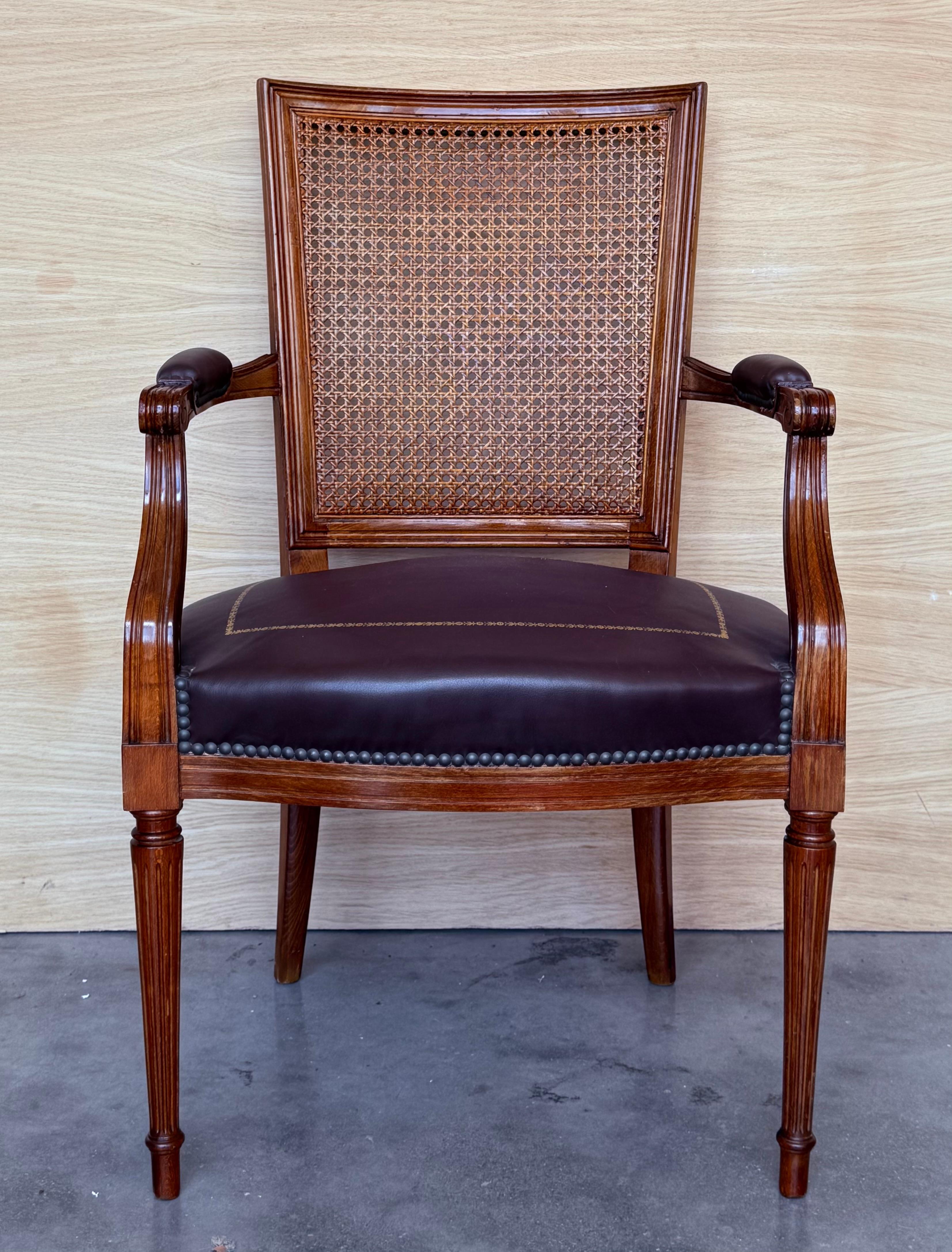 Fauteuil de style Louis XVI, sculpté dans le goût néoclassique, avec un dossier en rotin. Cadre très sculpté et moulé avec un ruban en guise d'accent. Le dossier canné et l'assise en cuir sont soutenus par des pieds cannelés et des pieds toupies. 
