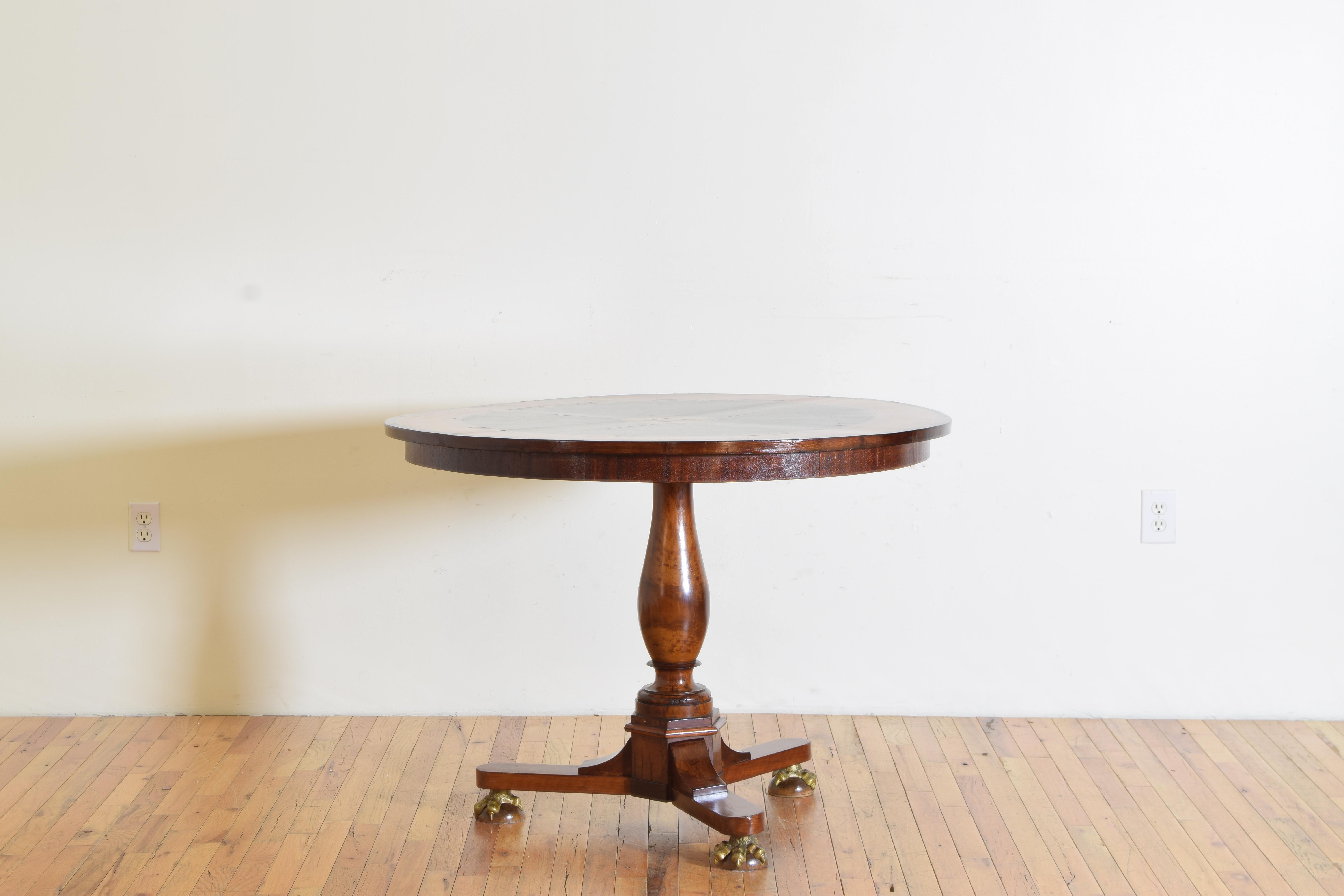 Having a round top covered in various veneers forming concentric rings from a centered sphere, the top reinforced with a hidden steel support, a solid wooden standard atop a shaped tripartite base raised on brass claw feet atop balls, either
