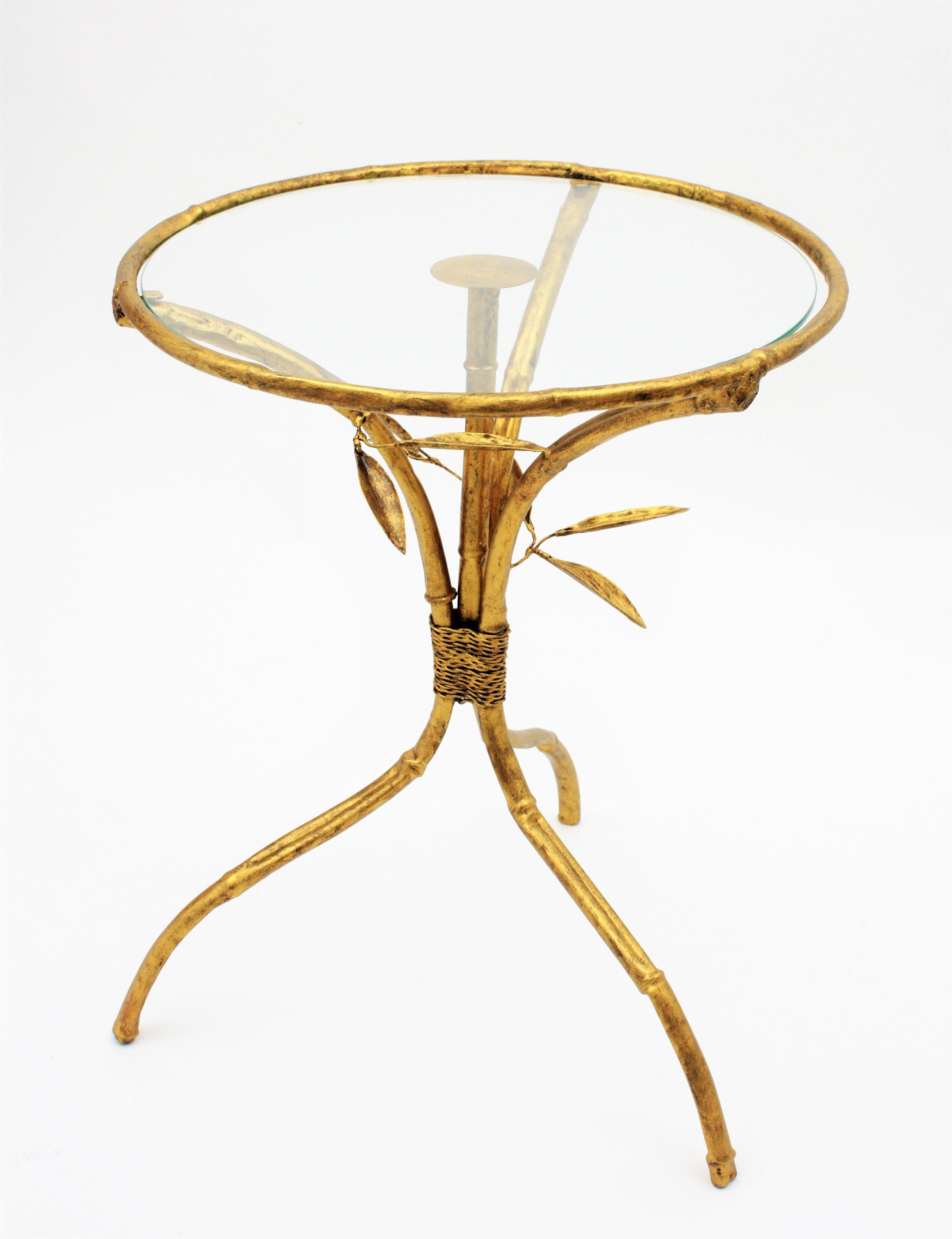 Eye-catching Hollywood Regency gilt iron faux bamboo gueridon drinks table with foliage details, Spain, 1950s. 
This beautiful round table stands up on three legs with a beautiful faux bamboo design. Leaf decorations and rope details joining its