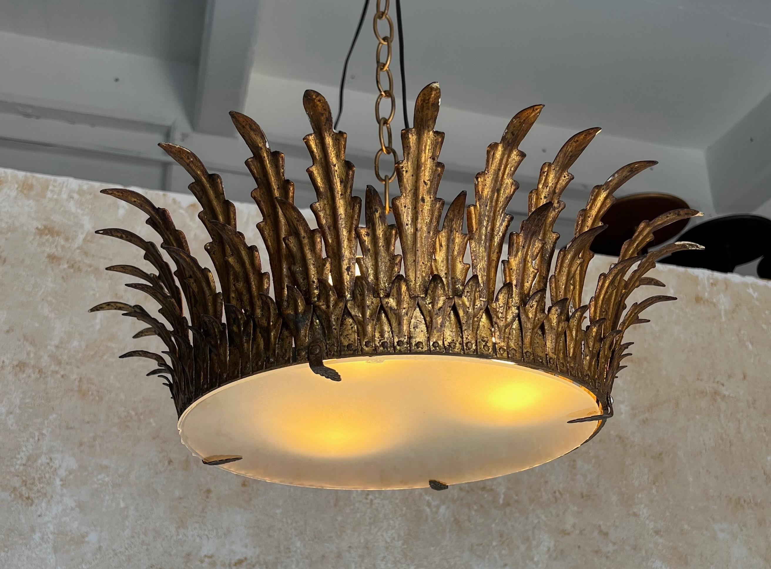 Ce plafonnier unique à grande couronne présente les caractéristiques suivantes  trois rangées de rayons de feuilles ou de plumes élégamment stylisées qui est non seulement élégant mais aussi pratique. Le travail du métal présente une riche finition