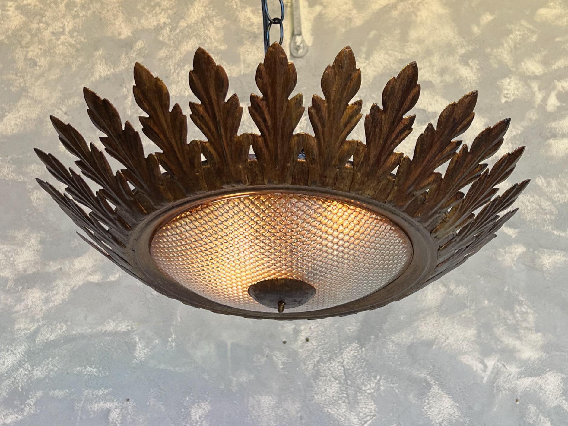 A simple but elegant Spanish flush mount ceiling fixture with a convex textured glass globe framed in evenly spaced leaves that gently curve upwards. The original gilt finish gives it an old world appeal. With a diameter of 16 inches and height of 4