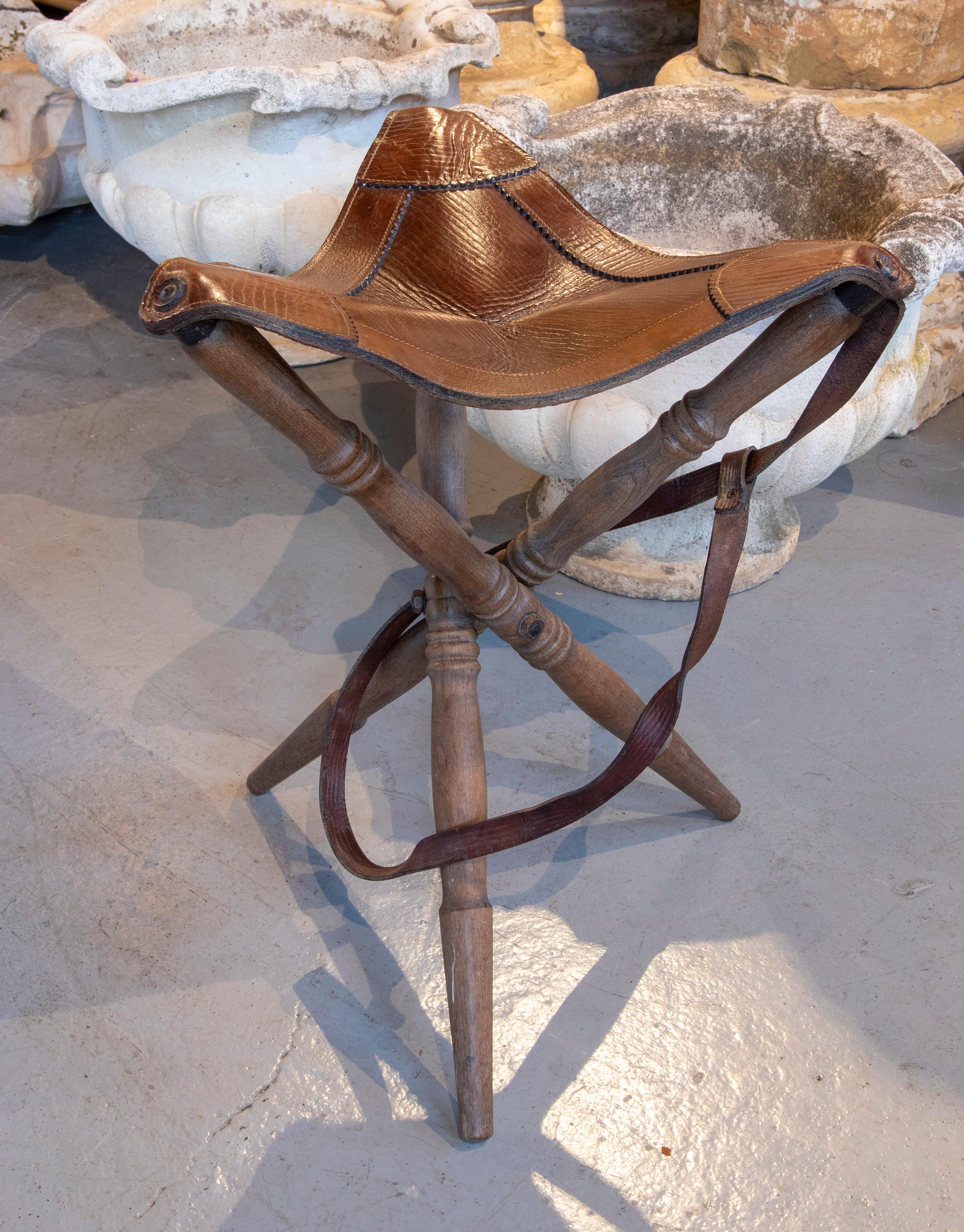 Spanish folding stool with wooden legs and leather seat.