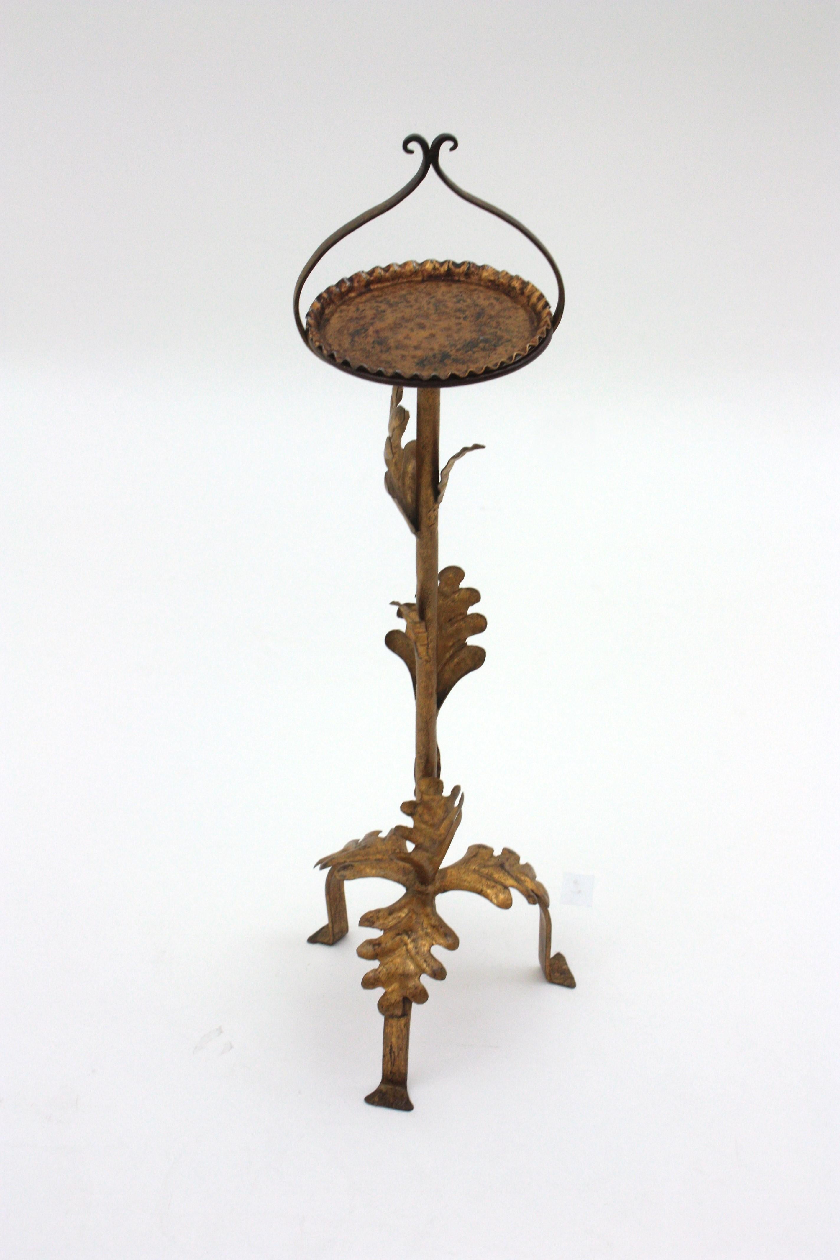 Vergoldeter schmiedeeiserner Getränketisch, Bodenaschenbecher, Dreibeinständer oder Sockel, 1940er Jahre.
Ein stilvoller, handgehämmerter Aschenbecher aus Eisen mit Laubmotiv, gewelltem Deckel und Griff.
Sie steht auf einem dreibeinigen Sockel mit