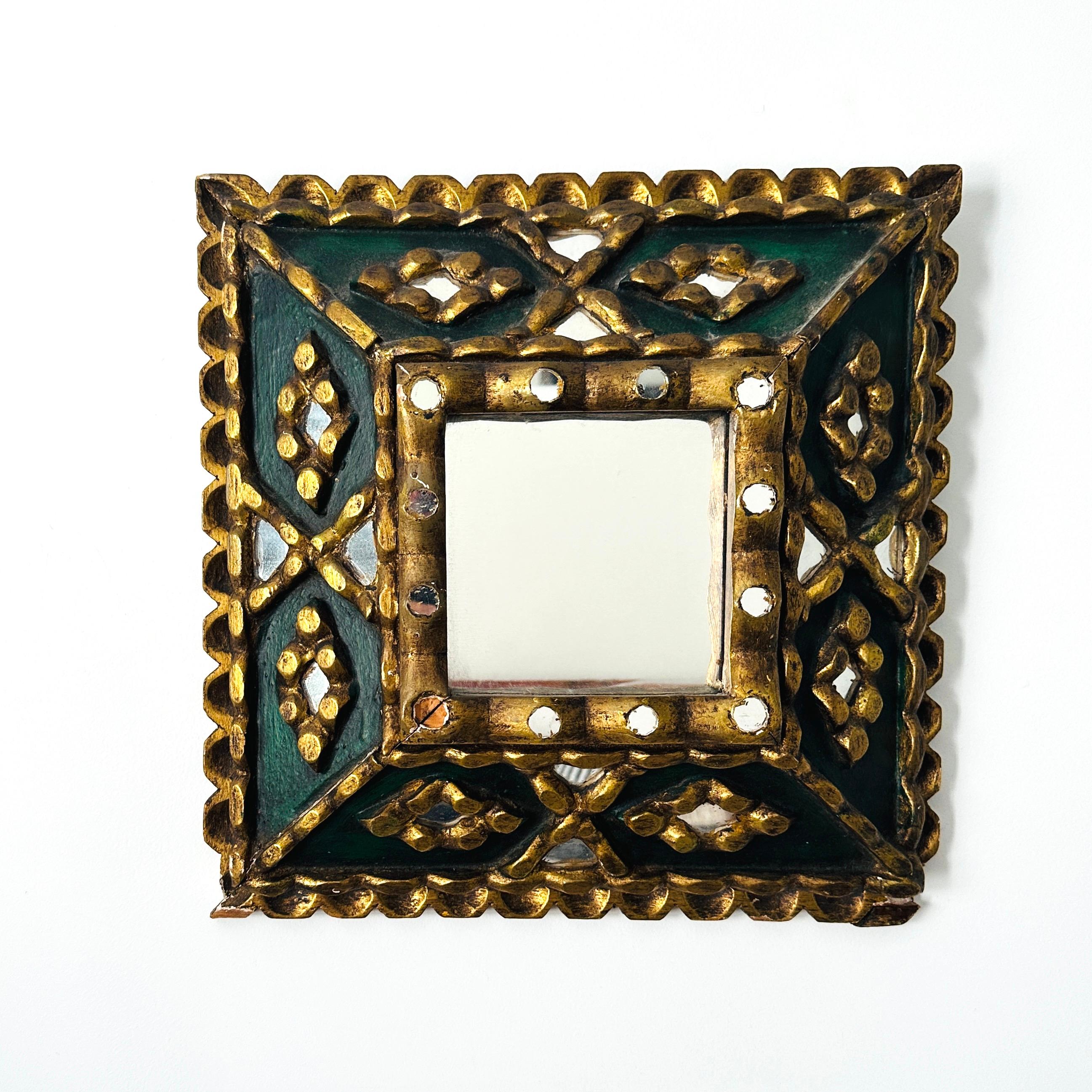 Antique Spanish Colonial mirror features a handmade shadowbox frame with ornate hand carvings  in gilt wood.  This unique frame also features a series of mosaic mirrored insets and a hand-painted center in dark green.  Missing one mirror inset and