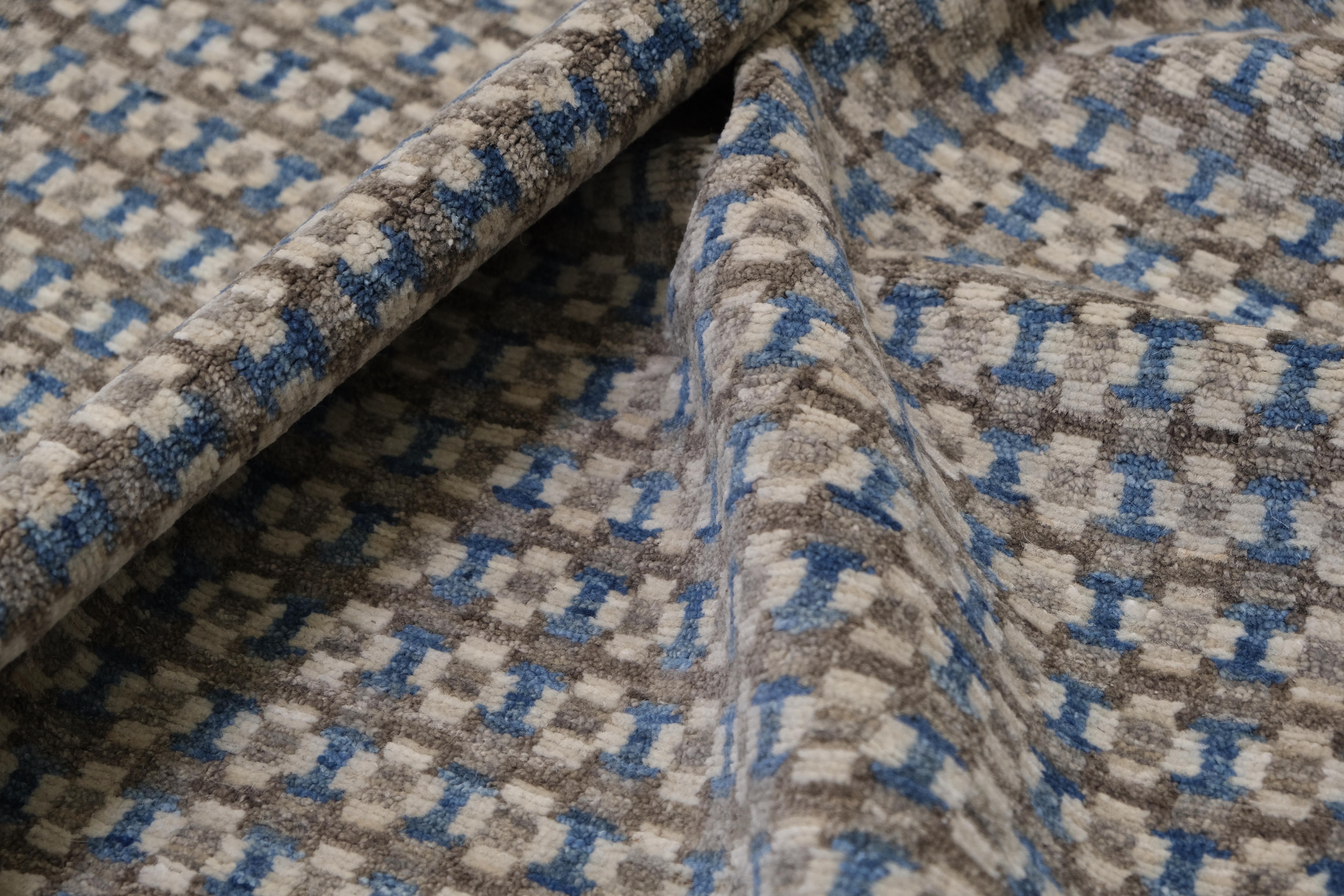 Dieser exquisite, handgeknüpfte Wollteppich mit seinem fesselnden geometrischen Muster wertet Ihre Einrichtung auf. Eine harmonische Farbpalette aus sanften Blautönen, warmen Grautönen und Braun schafft ein optisch ansprechendes Gleichgewicht und