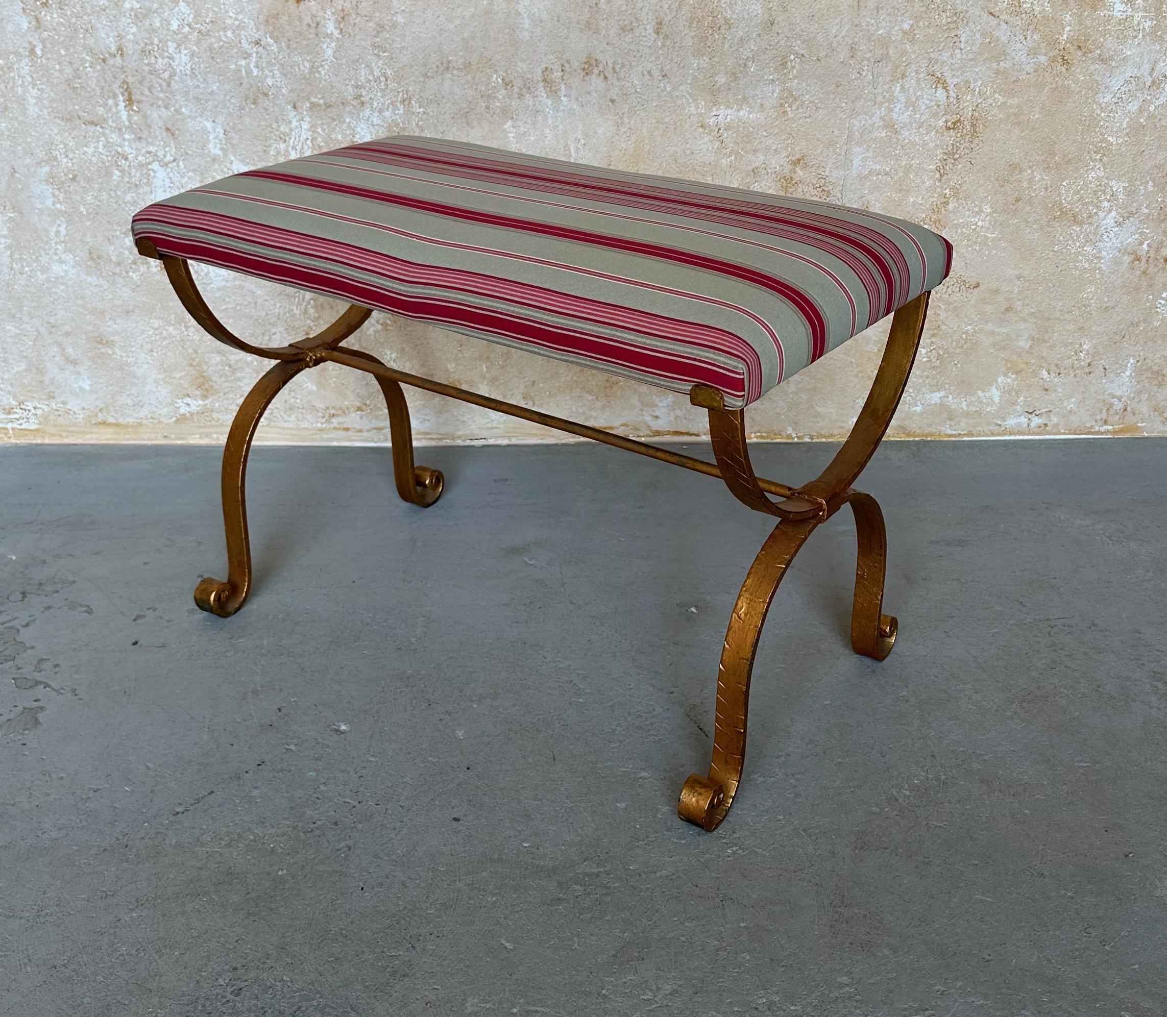 This lovely Spanish gilt iron bench features a hammered hourglass frame with scrolled legs. The seat has been recently reupholstered in fashionable striped red and gray fabric. In very good condition, this piece is sure to be as durable as it is