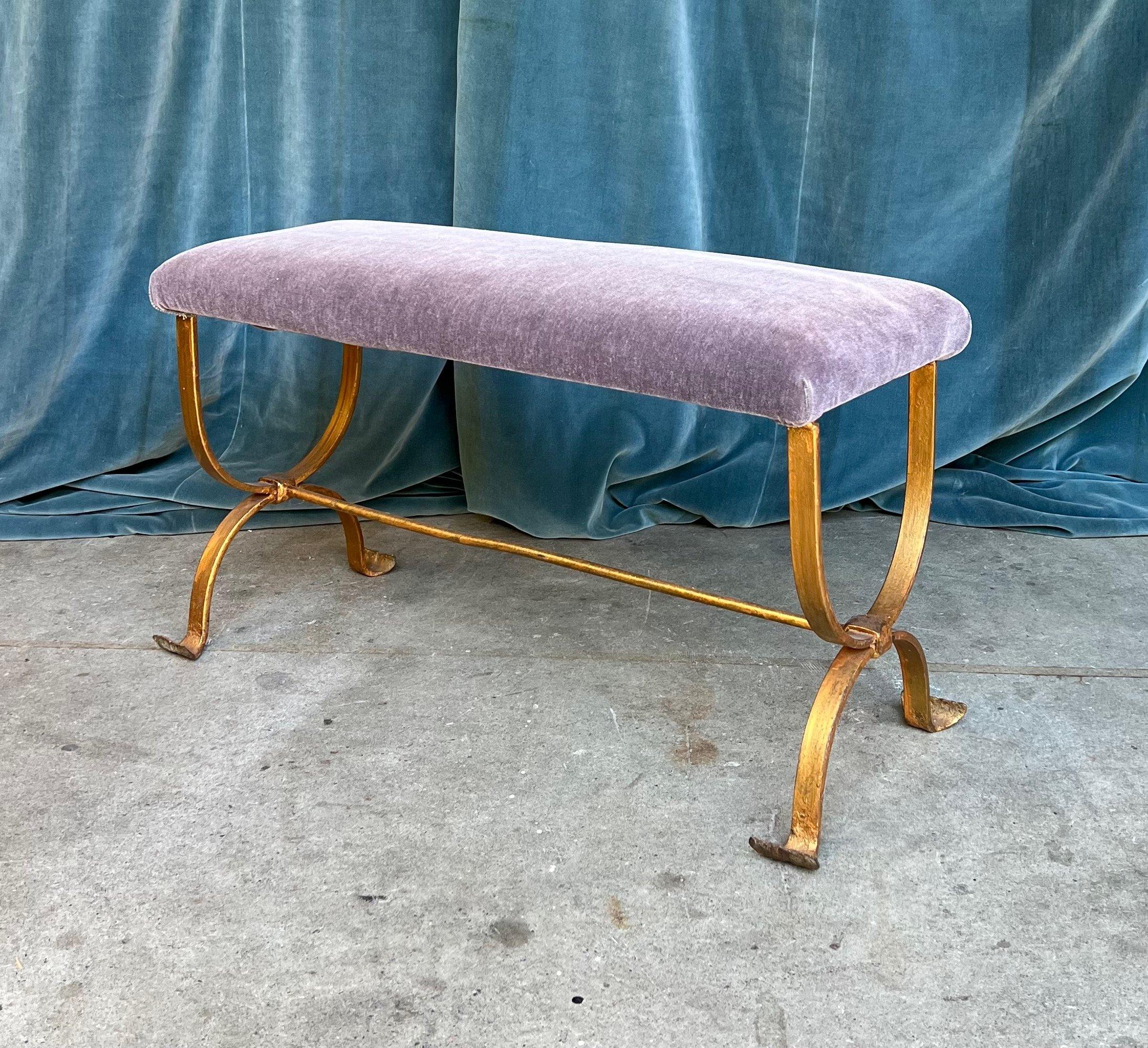 This Spanish 1950s gilt iron bench embodies a vintage charm that is timeless as well as modern. Its hourglass frame, central stretcher, and gently curved feet each contribute to its unique appeal. The brilliant gilt  finish, achieved through a