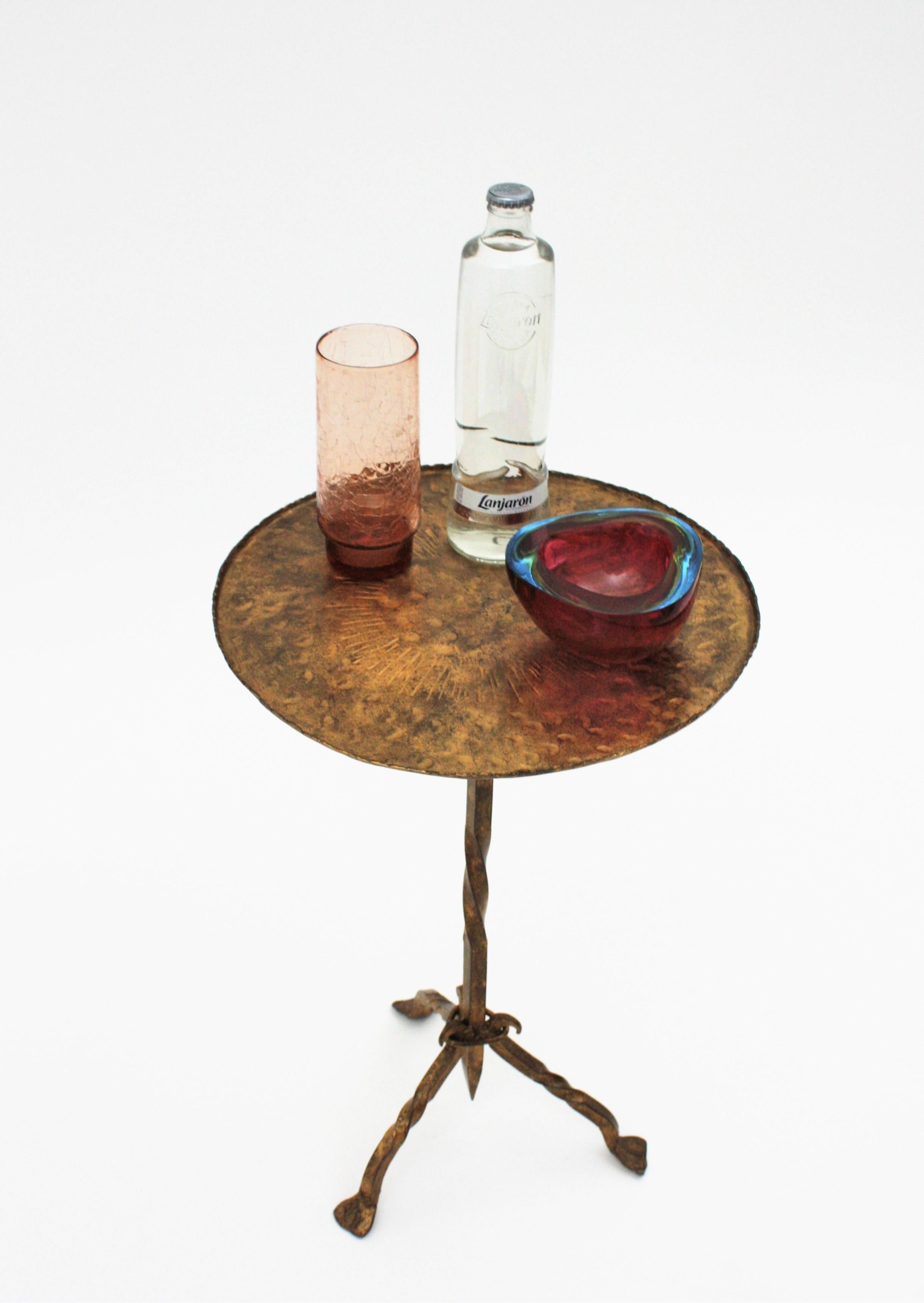 Beautiful hand-hammered gilt wrought iron occasional drinks table on a tripod base, Spain, 1940s-1950s.
This guéridon was handcrafted at the Mid-Century Modern period with Gothic style accents. It has a decoration with hammered stripe marks on the