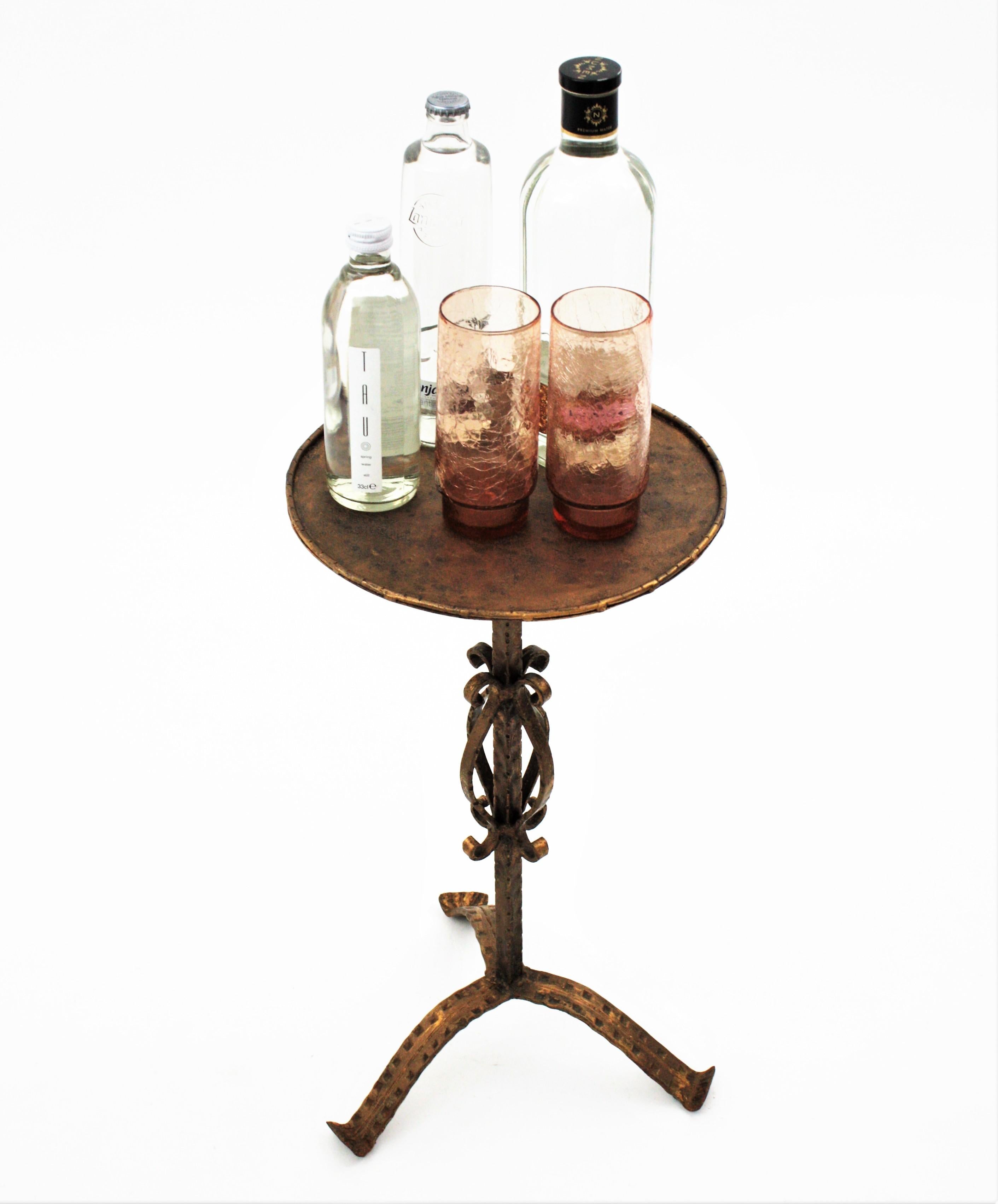 Eye-catching hand-hammered iron Guéridon / end or side table with bronze-gilt patina and ornamented base. Spain, 1950s-1960s.
The round top stands on a tripod base ornamented with scroll motifs. The feet of this Martini table are richly decorated