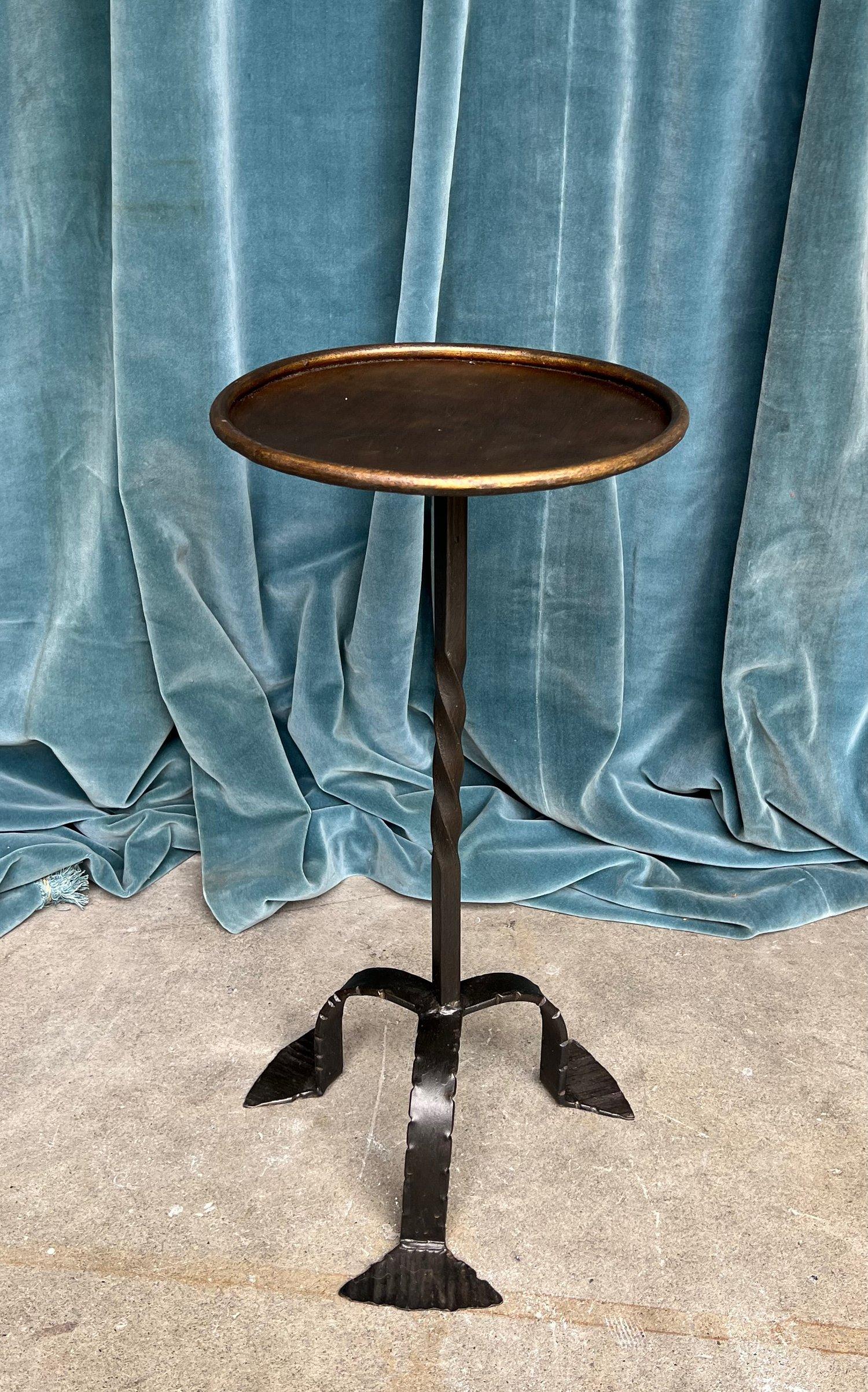 This Spanish drinks table is a unique piece distinguished by its painted black base and patinated gilt top. The table stands on a black-painted tripod base with a twisted stem, lending it a distinct vintage appeal. Its standout feature is the