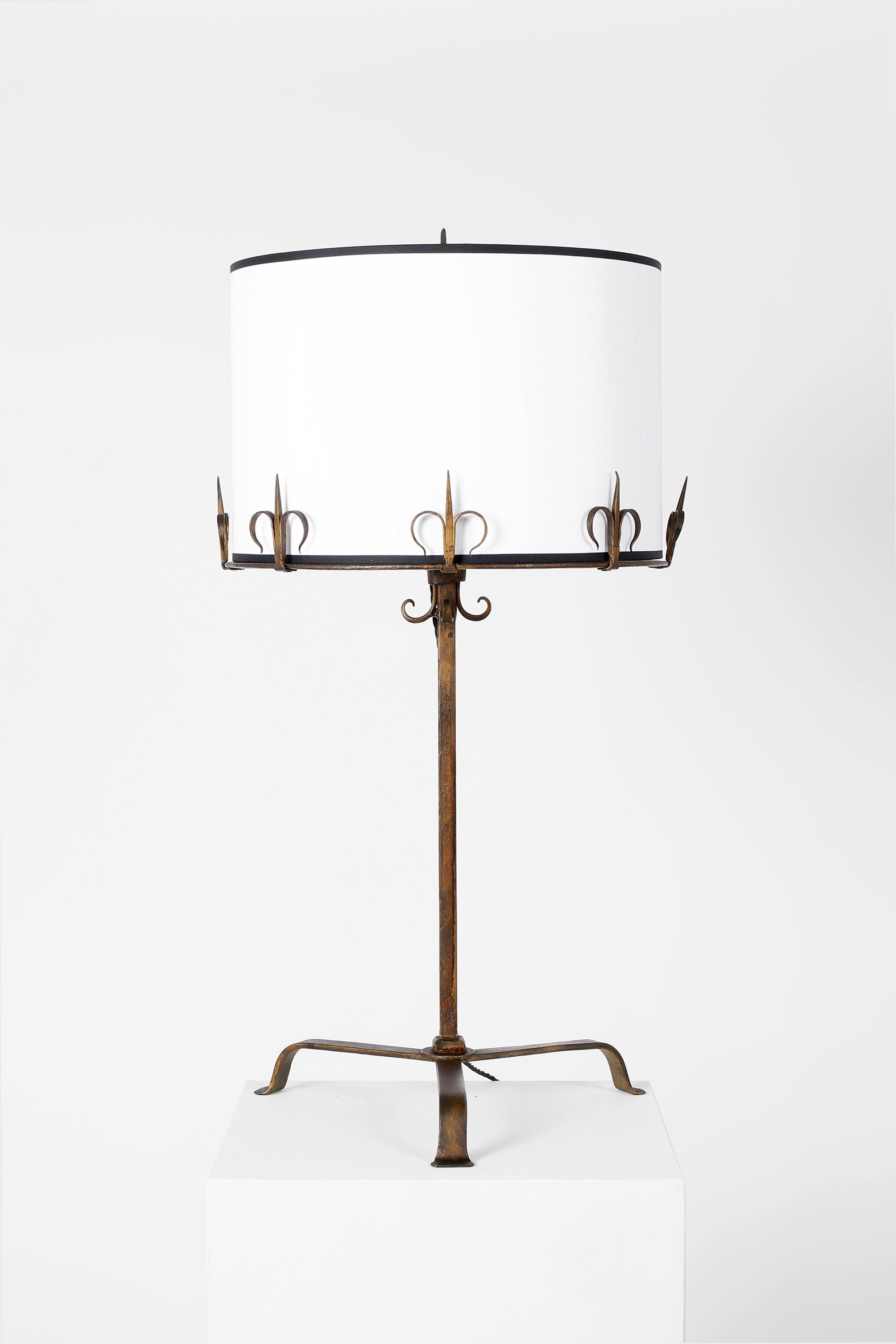 A run of seven gilt forged iron table lamps in the taste of Les Artisans de Marolles, with decorative fleur-de-lis detailing, three point bases and new white cotton shades with black trim. From a hotel in Andalusia, southern Spain, c. 1960.