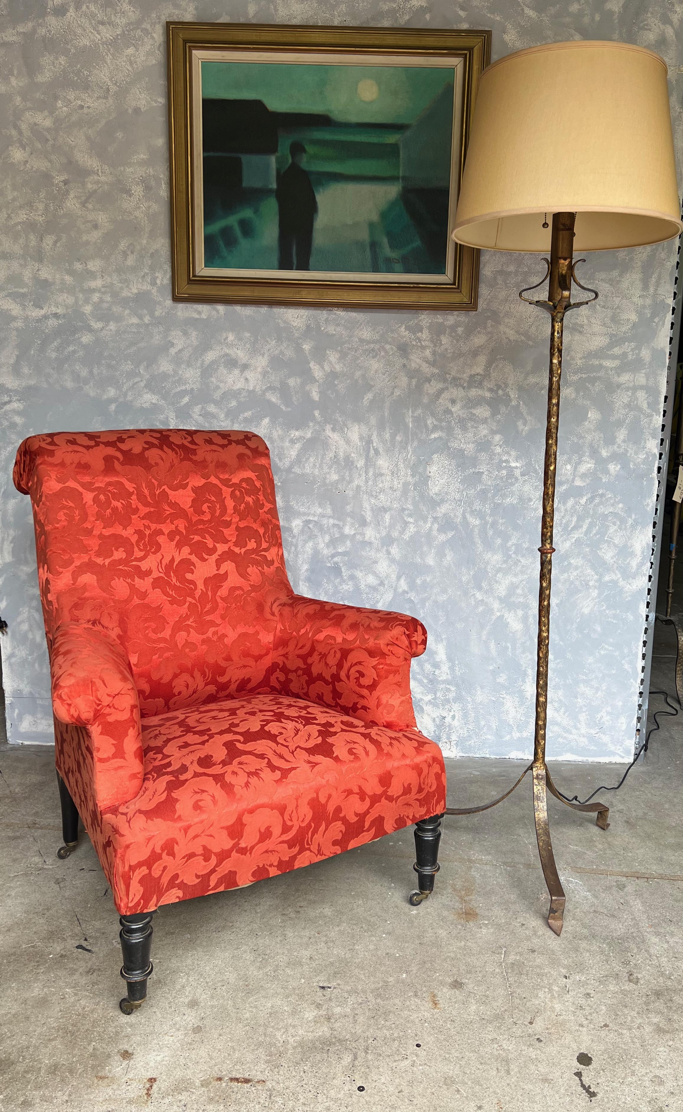 This Spanish gilt iron floor lamp, dating back to the 1950s, is a distinctive piece with its elevated tripod base. The lamp possesses an aged darkened gold patina that adds character and an air of antiquity. The stem's upper part features a hammered