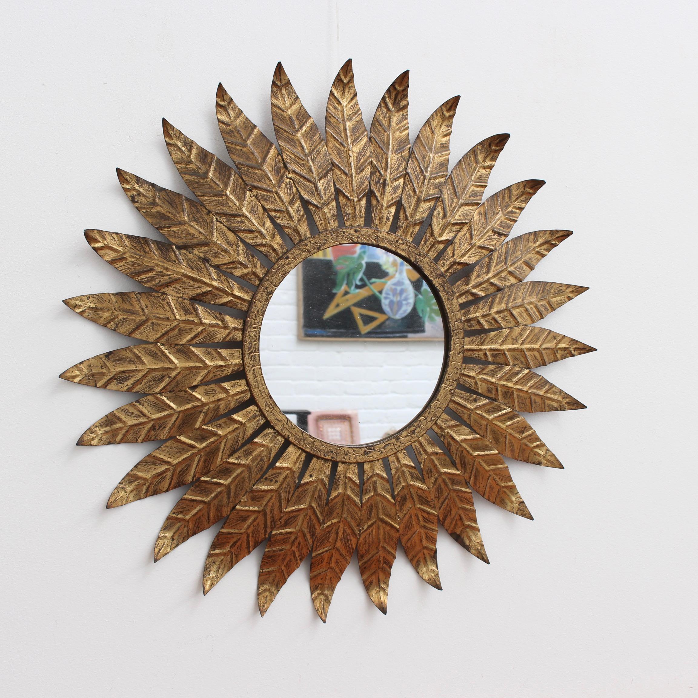 Spanish gilt metal sunburst mirror (circa 1960s) with leaf motif rays emanating from the glass border. In fair vintage condition commensurate with age and use. Some authentic age spots and characterful markings appear on gilt surface adding