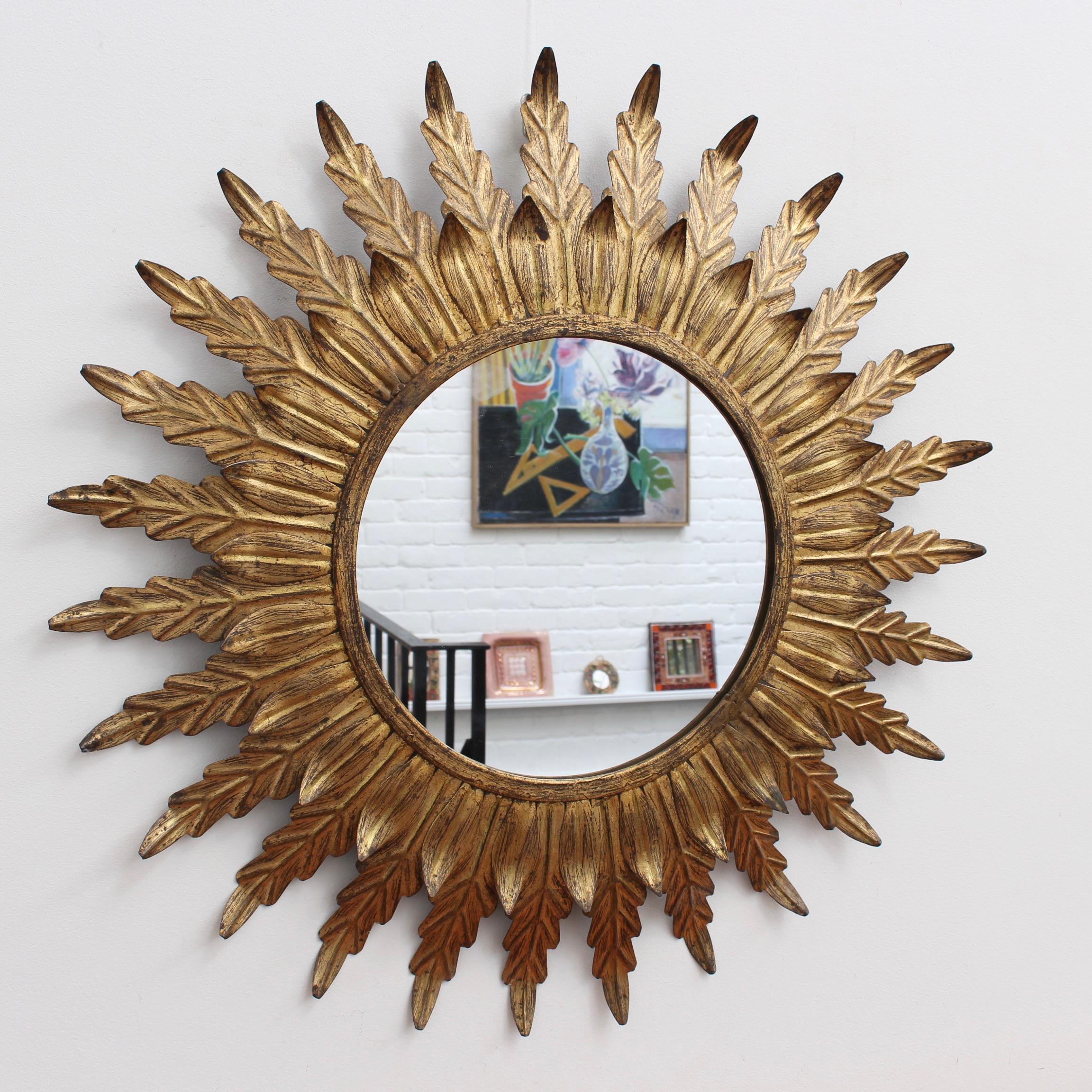 Spanish gilt metal sunburst mirror (circa 1960s) with leaf motif rays emanating from the glass border. In fair vintage condition commensurate with age and use. Some authentic age spots and characterful markings appear on gilt surface and underside