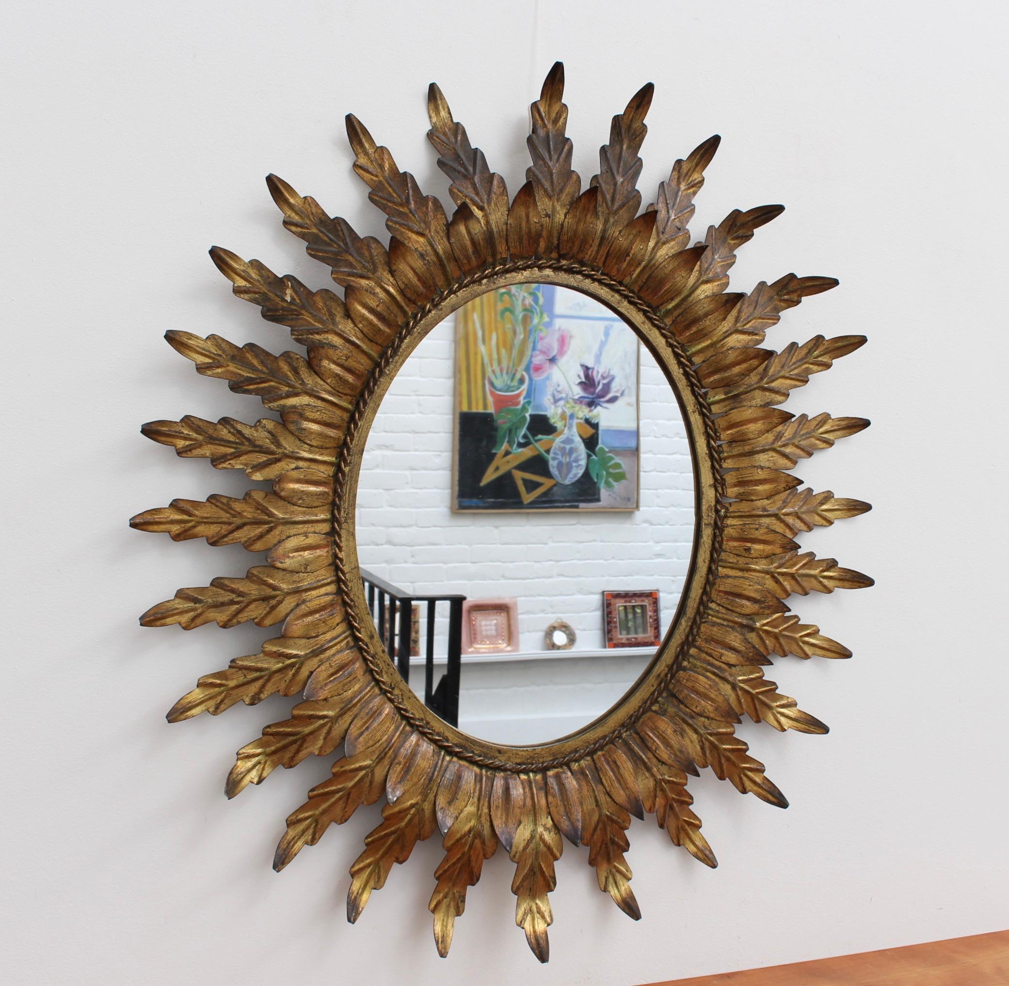 Spanish gilt metal sunburst mirror (circa 1960s) with leaf motif rays emanating from the glass border with rope design. In fair vintage condition commensurate with age and use. Some authentic age spots and characterful markings appear on gilt