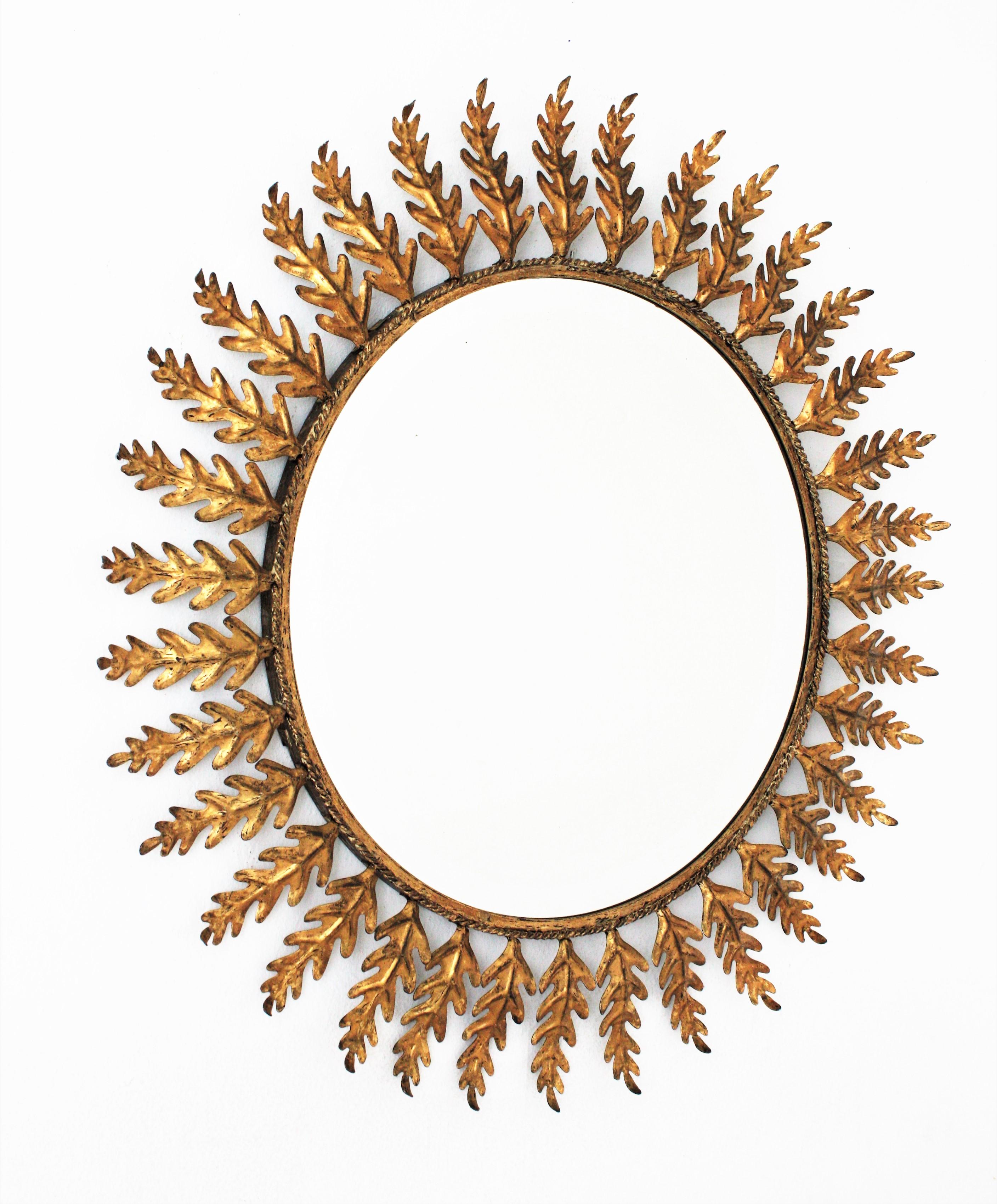 Outstanding gold leaf gilt iron sunburst mirror framed by oak leaves. Spain, 1960s.
This round sunburst mirror has a lefed frame comprised by oak leaves handcrafted in iron and gilded with gold leaf.
It has a beautiful design, a large mirror surface