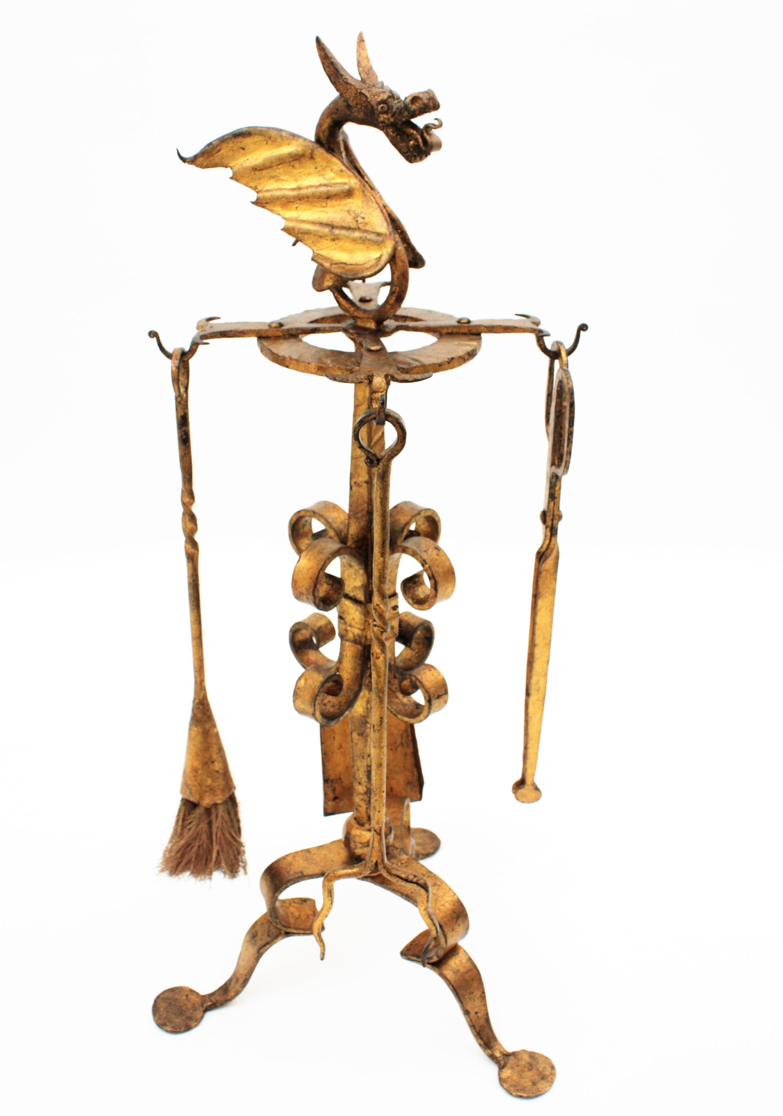 Spanish hand forged iron four-piece fireplace tool set Stand with scrolls ornamentation, dragon motif and original gold leaf gilt finishing. Spain, 1920s-1930s.
This sculptural tools set holds on a tripod base Stand with scrolls ornamentations and a