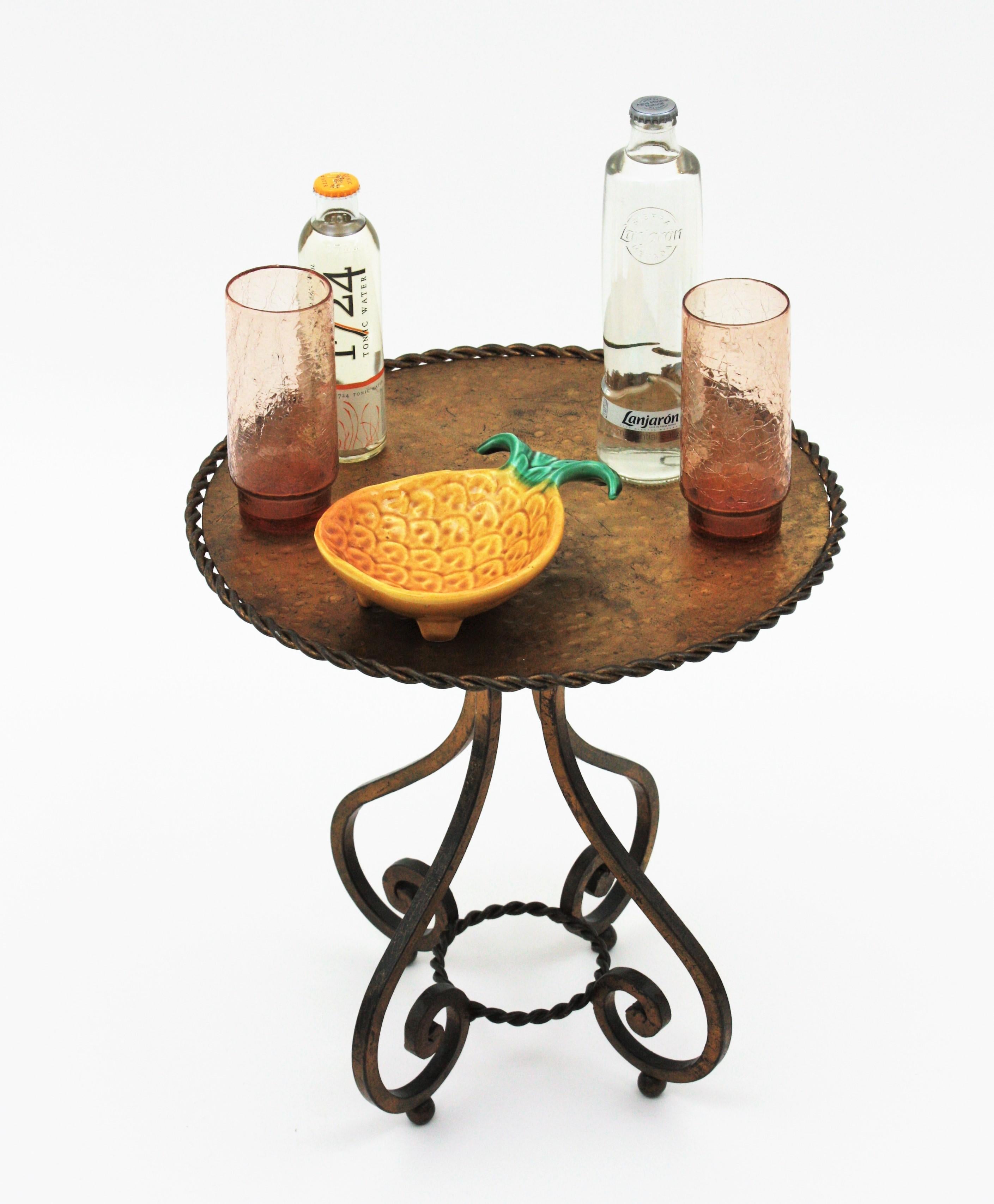 Elegant wrought gilt iron low round coffee table or occassional table drinks table. Spain, 1920s
This drink table stands up on four scrolled legs supported on iron balls . The top is heavily adorned by the Hammer marks and it has braided iron rope