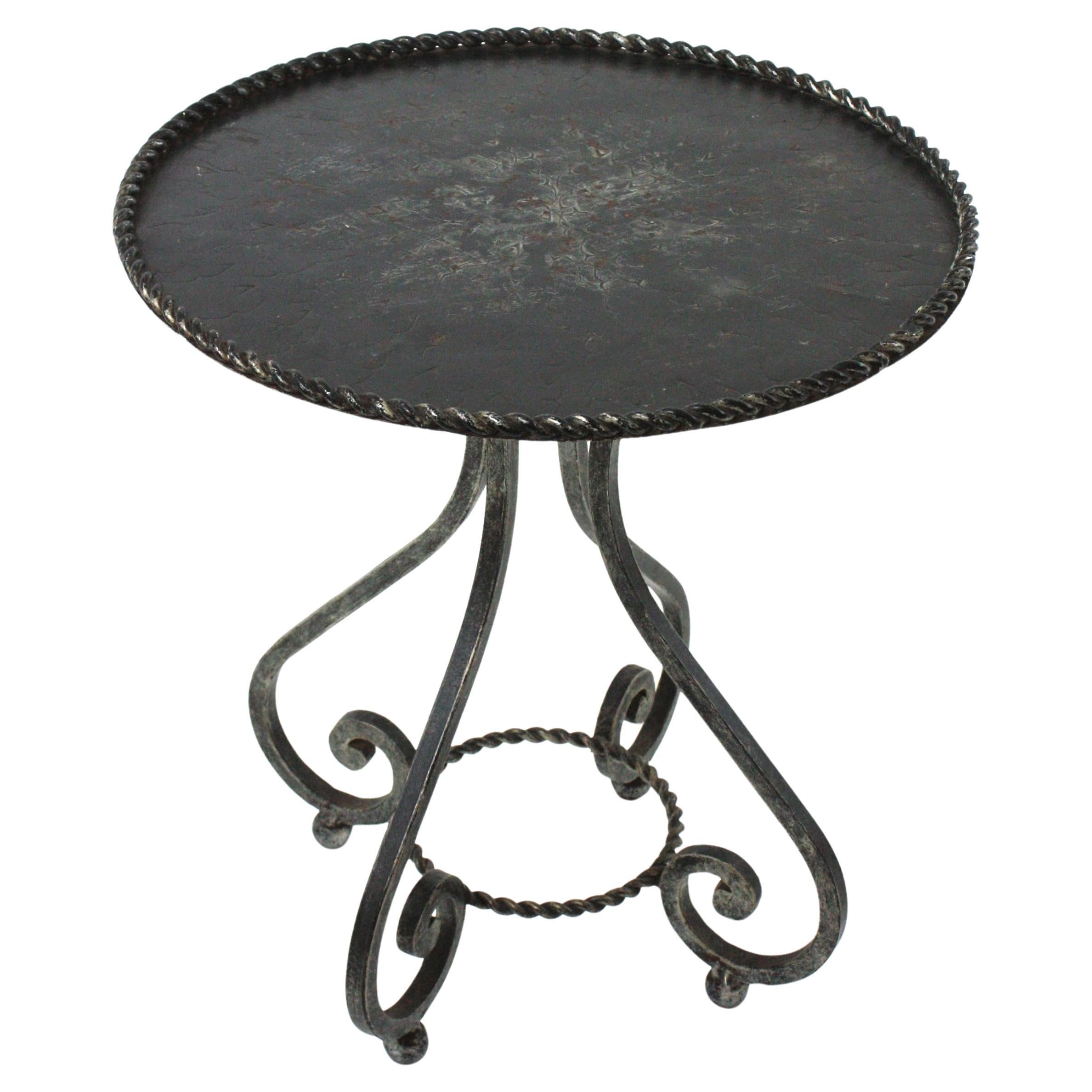 Elegant wrought iron low round coffee table or occassional table drinks table. Spain, 1940s
This drink table stands up on four scrolled legs supported on iron balls . The top is heavily adorned by the hammer marks and it has braided iron rope