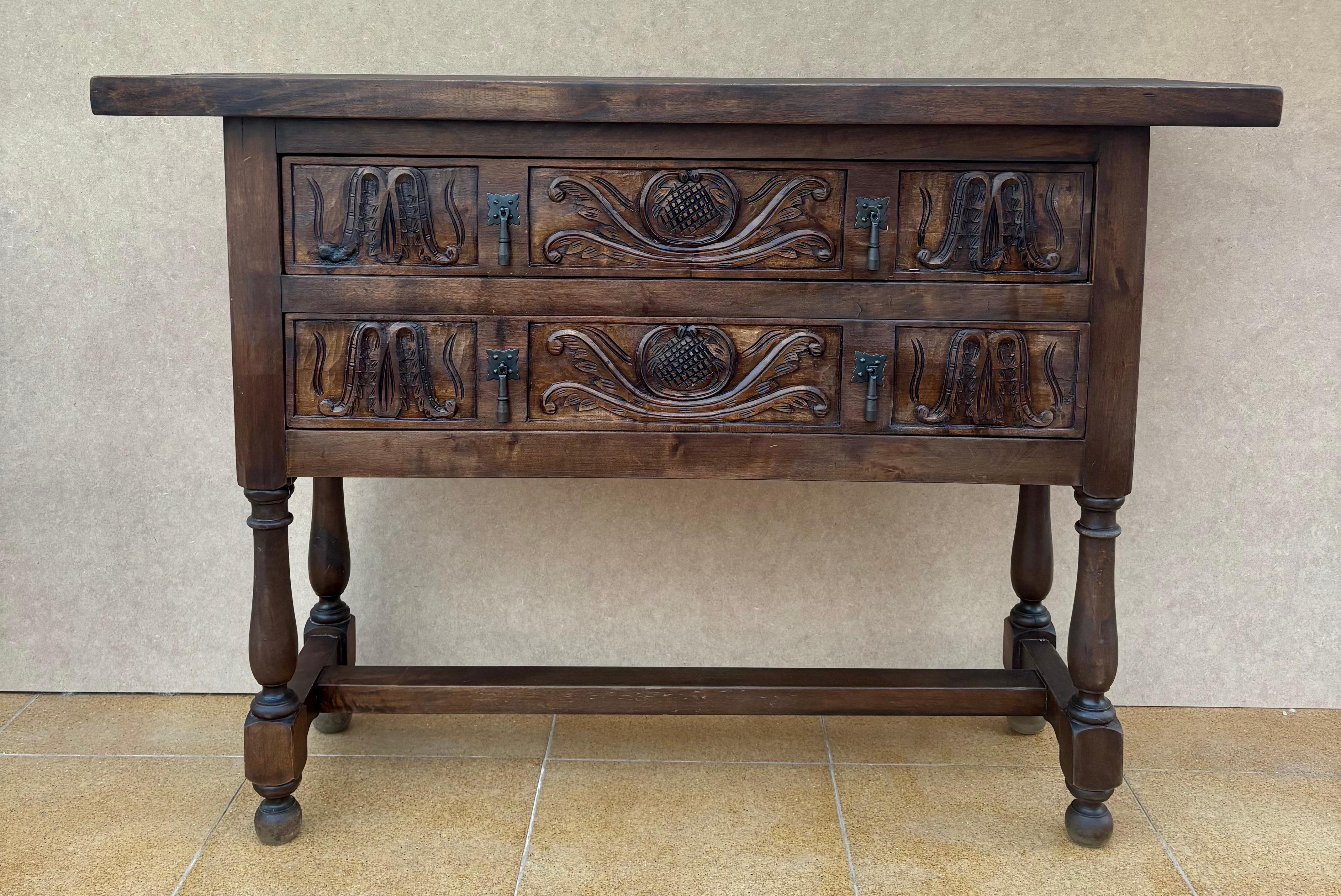 Consola de nogal de principios del siglo XX con tablero sobre friso con dos frentes de cajón decorados con talla con decoración adicional y dos tiradores originales de hierro en cada cajón. La mesa descansa sobre una base tallada a mano con patas