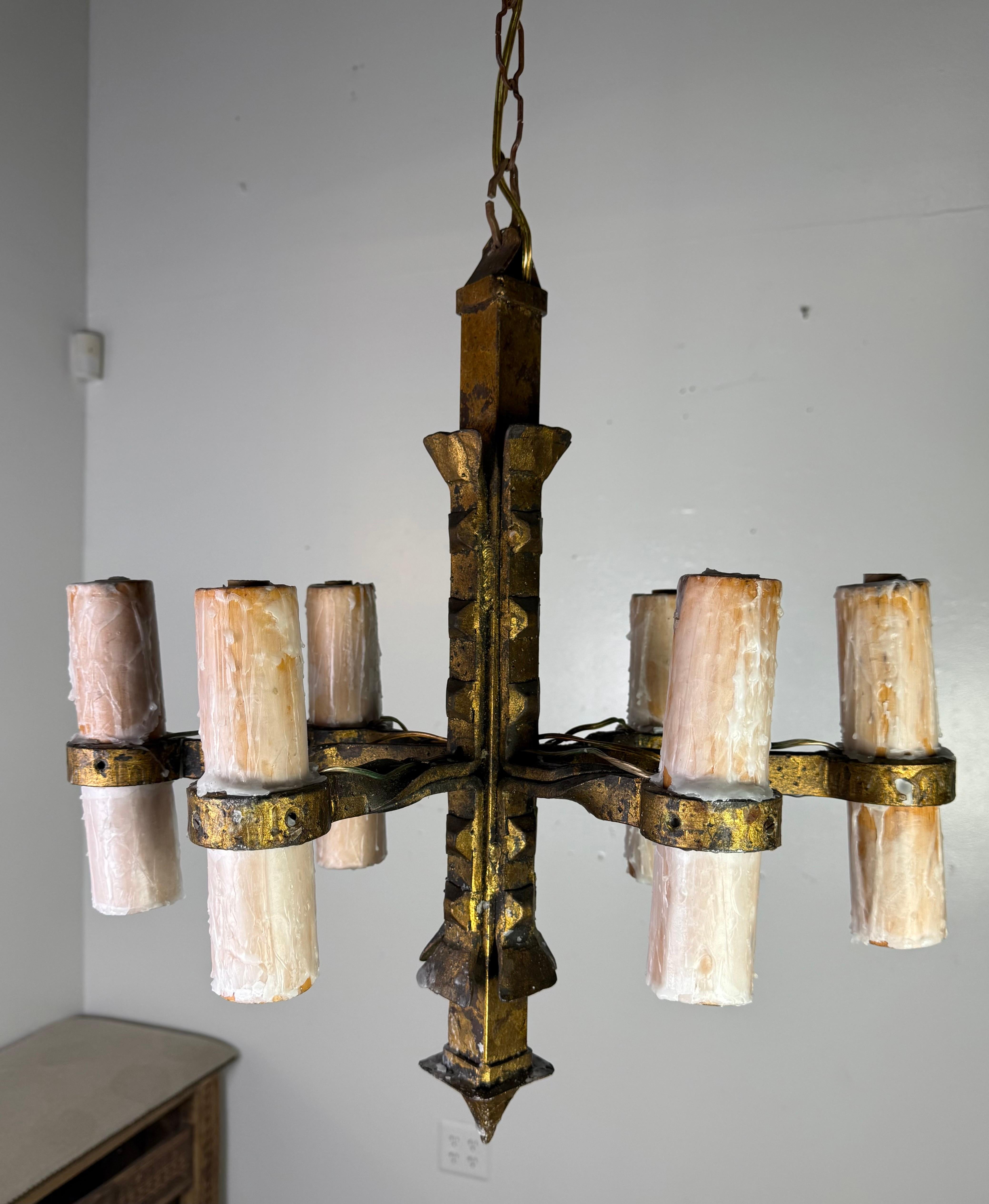 Ce lustre à six lumières est un exemple frappant d'artisanat rustique forgé à la main avec une silhouette géométrique audacieuse. Fabriquée en fer lourd, cette pièce présente une patine sombre et vieillie accentuée par des touches de dorure,