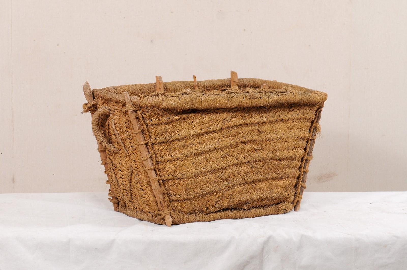 A Spanish handwoven basket with lid from the mid-20th century. This vintage basket from Spain has a trapezoid-shaped body and is handwoven and braided natural fibers with stick supports set vertically at each corner and along it's backside. There