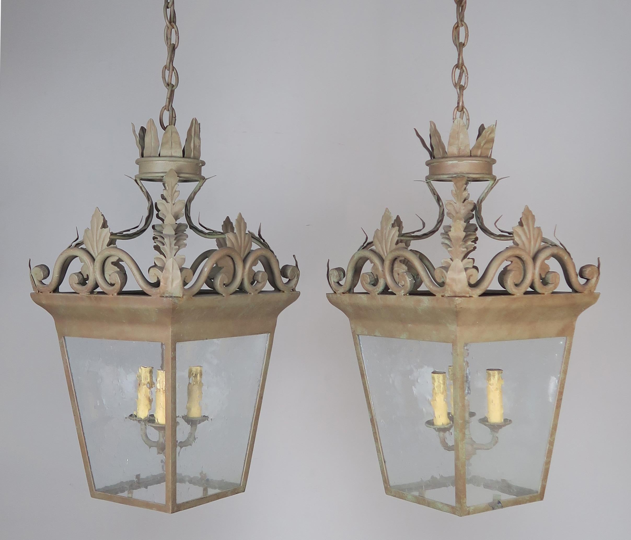 Pair of Spanish hand-wrought iron three-light lanterns with crown detail at top. This pair came from a Montecito home near Santa Barbara, California. The lanterns have the original pitted glass. Newly rewired including chain and canopy and ready to