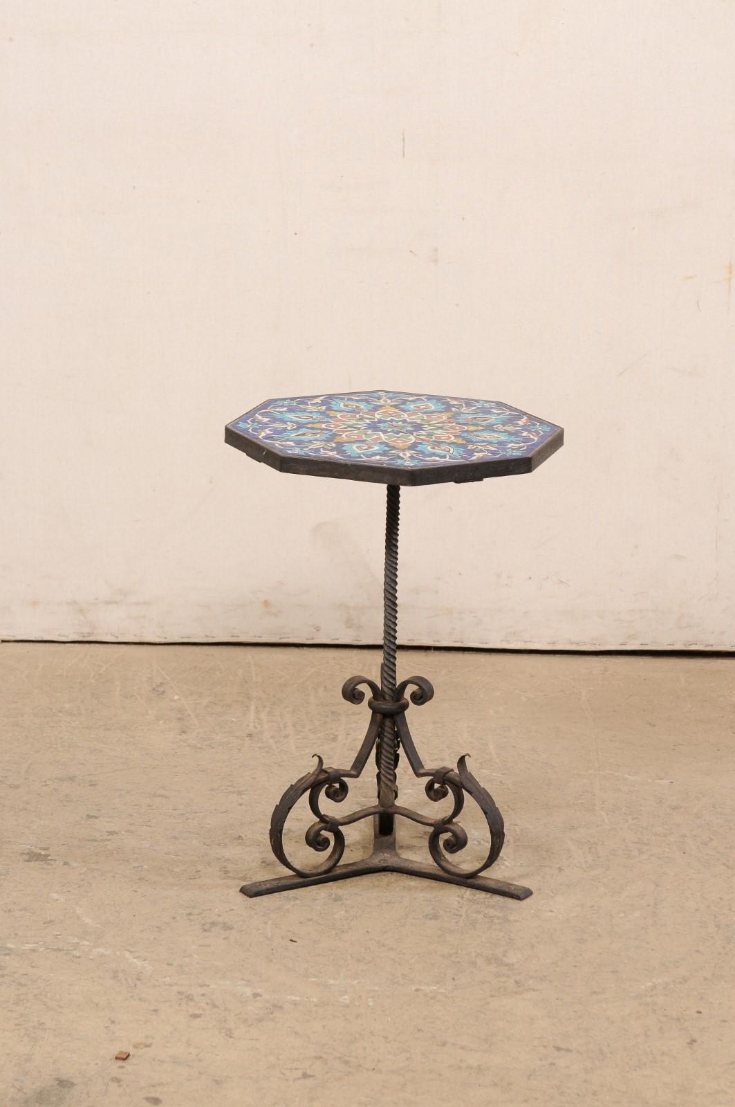 A Spanish tile top small size pedestal drinks table. This petite table from Spain has an octagonal shaped top with vibrant ceramic tiles recessed within the iron lip, raised upon a spiraled iron post, supported at the floor upon a triangular base