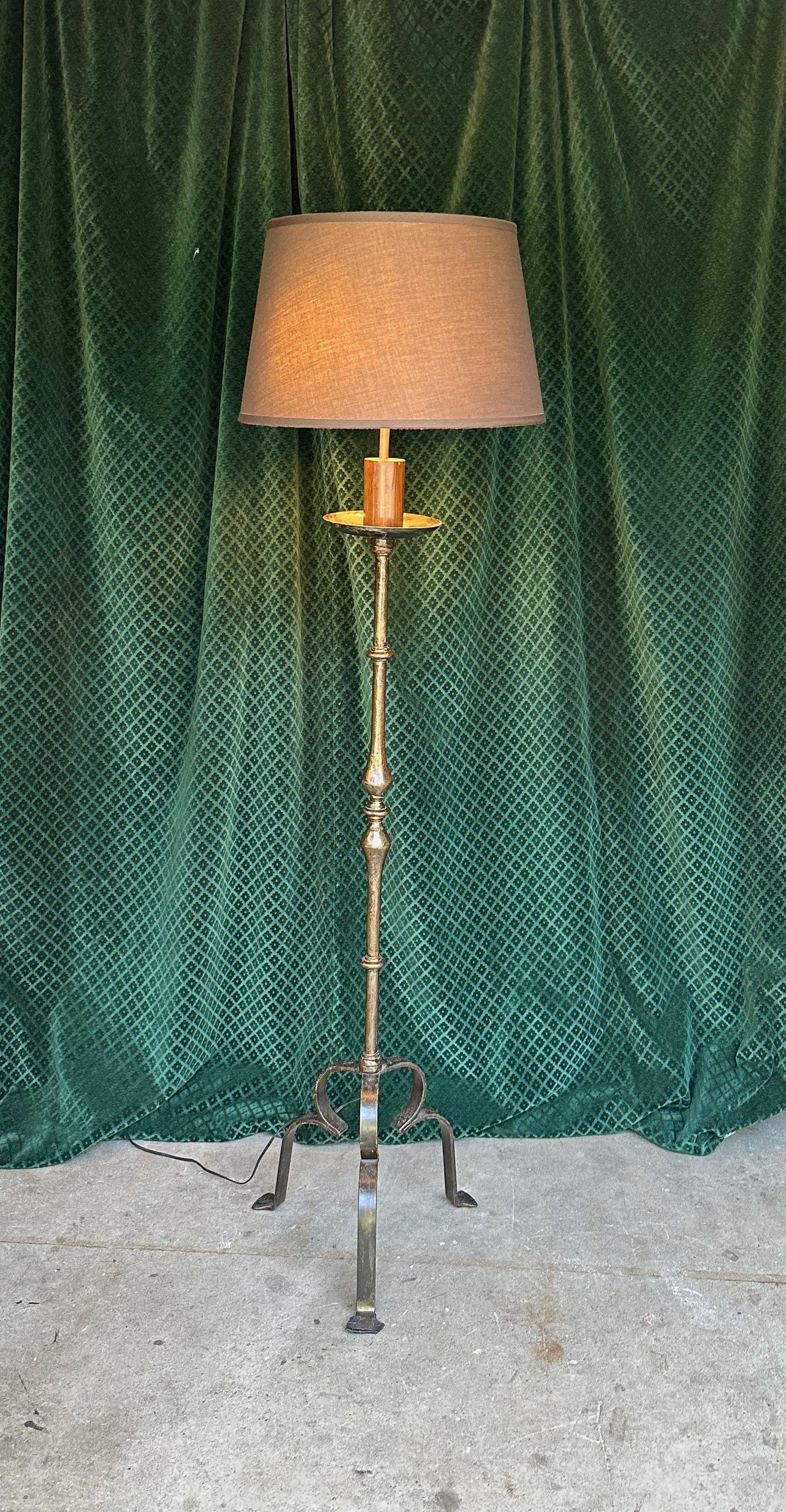 This remarkable wrought iron floor lamp is a striking embodiment of elegance and allure. Possessing a robust feel and a solid tripod base, the lamp reaches an impressive height of 67 inches with a 17 inch diameter base. The iron's rich patina lends