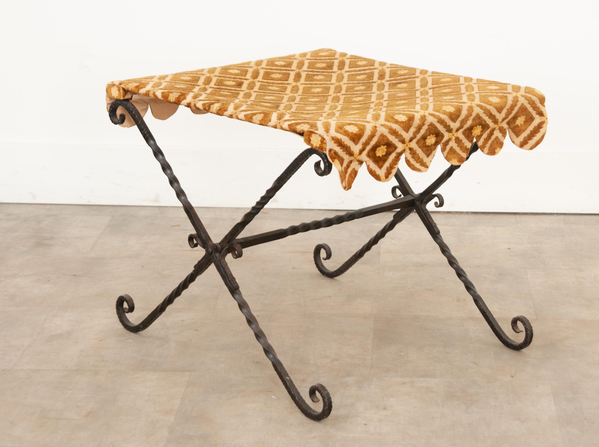A wonderful vintage hand forged wrought-iron folding stool with vintage scalloped edge fabric. A hand-forged twisty and curling X-base with connecting stretcher is topped with plush goldenrod colored fabric. For use as a portable seat or side table.