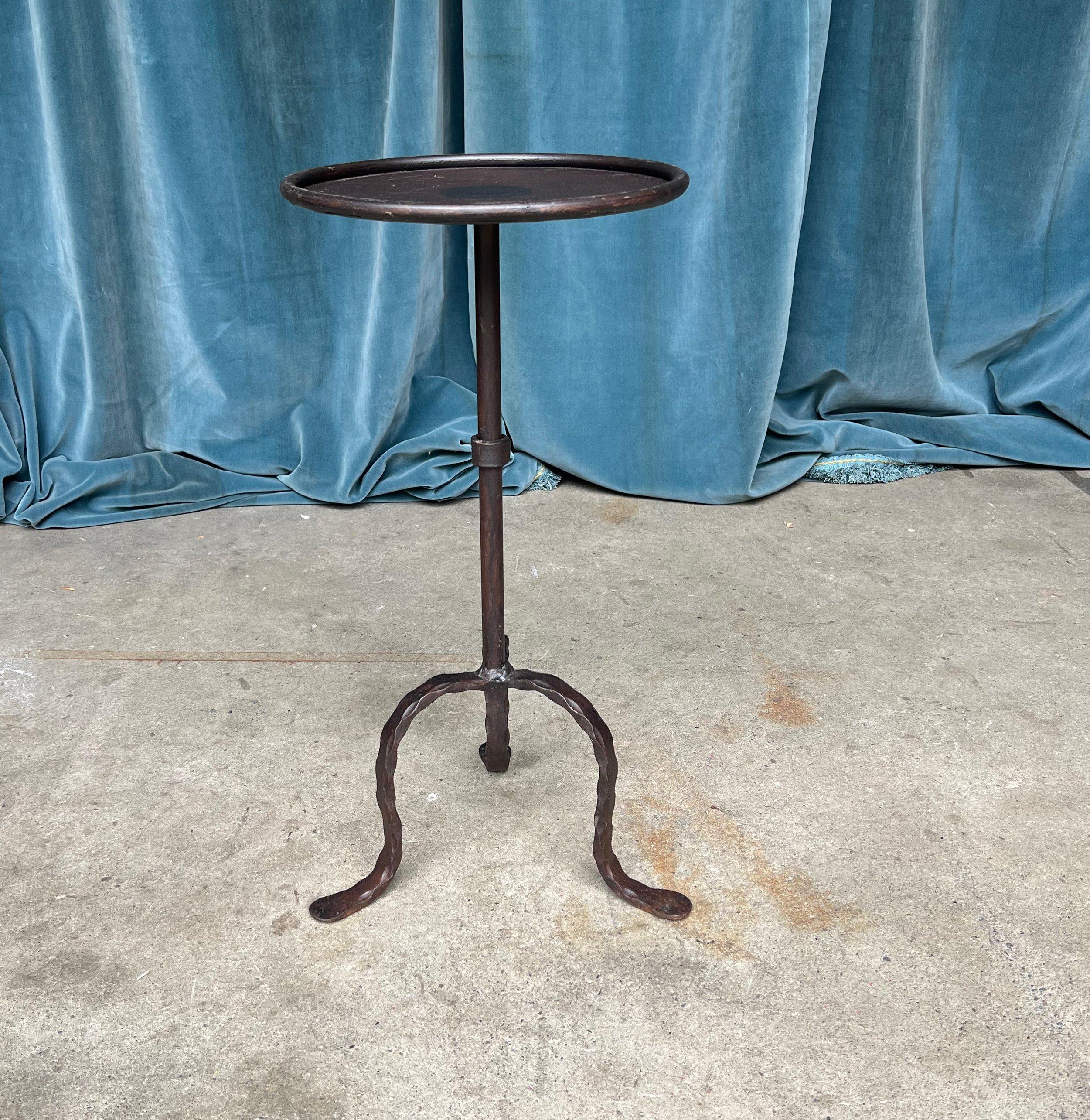 A charming small-scale Spanish iron drinks table from the 1950s, exuding elegance and vintage allure. The table features a circular central stem with a decorative collar accent, mounted on a tripod base with intriguing hammered effect legs. The