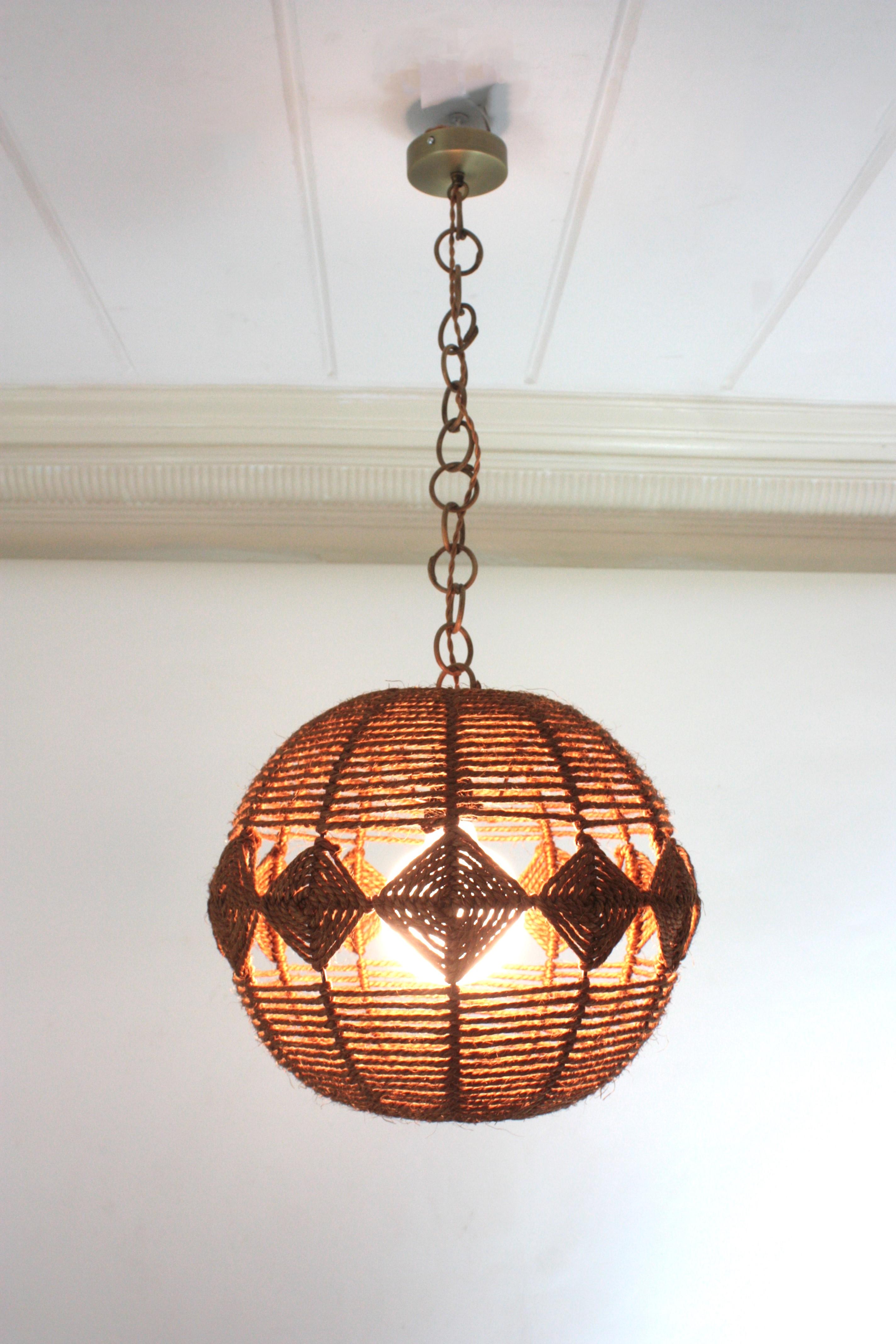 Eye-catching ball shaped rope pendant light with rhombus decorative details, Spain, 1960s
This midcentury suspension lamp features a hand woven rope shpere lampshade in brown ginger color accented by rhombus details. It hangs from a chain with