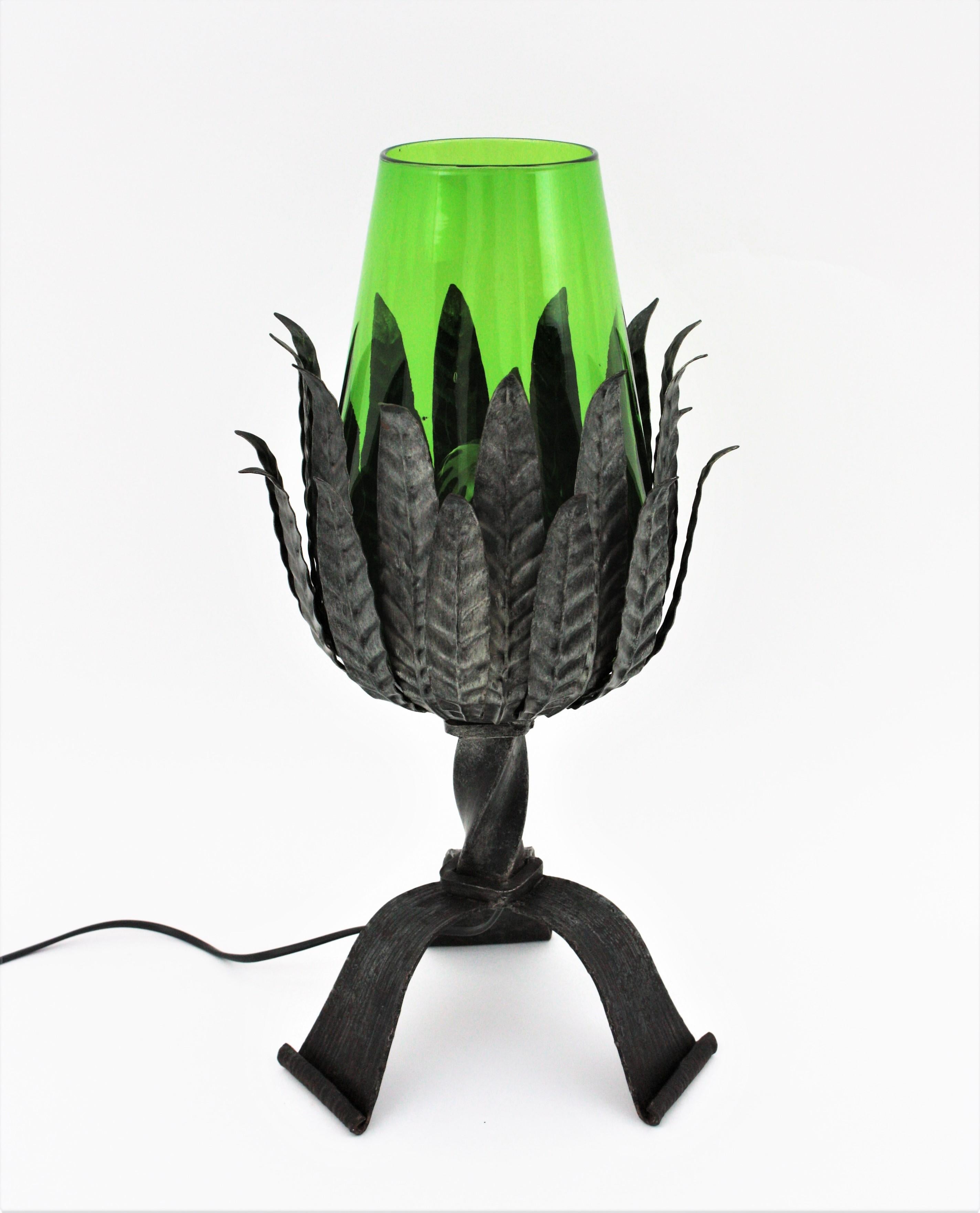 Silver patinated leafed iron table lamp with green glass lamphade. Spain, 1950s.
This gorgeous table lamp is entirely made by hand. This lamp features a bouquet of iron leaves holding a green blown glass lamphade. The base has a heavy construction