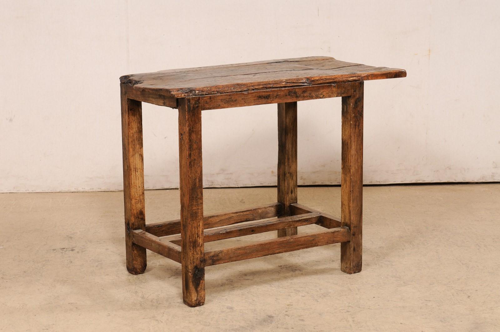 A Spanish rustic wooden accent table, with off-set top, from the turn of the 18th and 19th century. This antique table from France, with it's simplistic pastoral design, features a rectangular-shaped top, with live-edging in some areas and has been