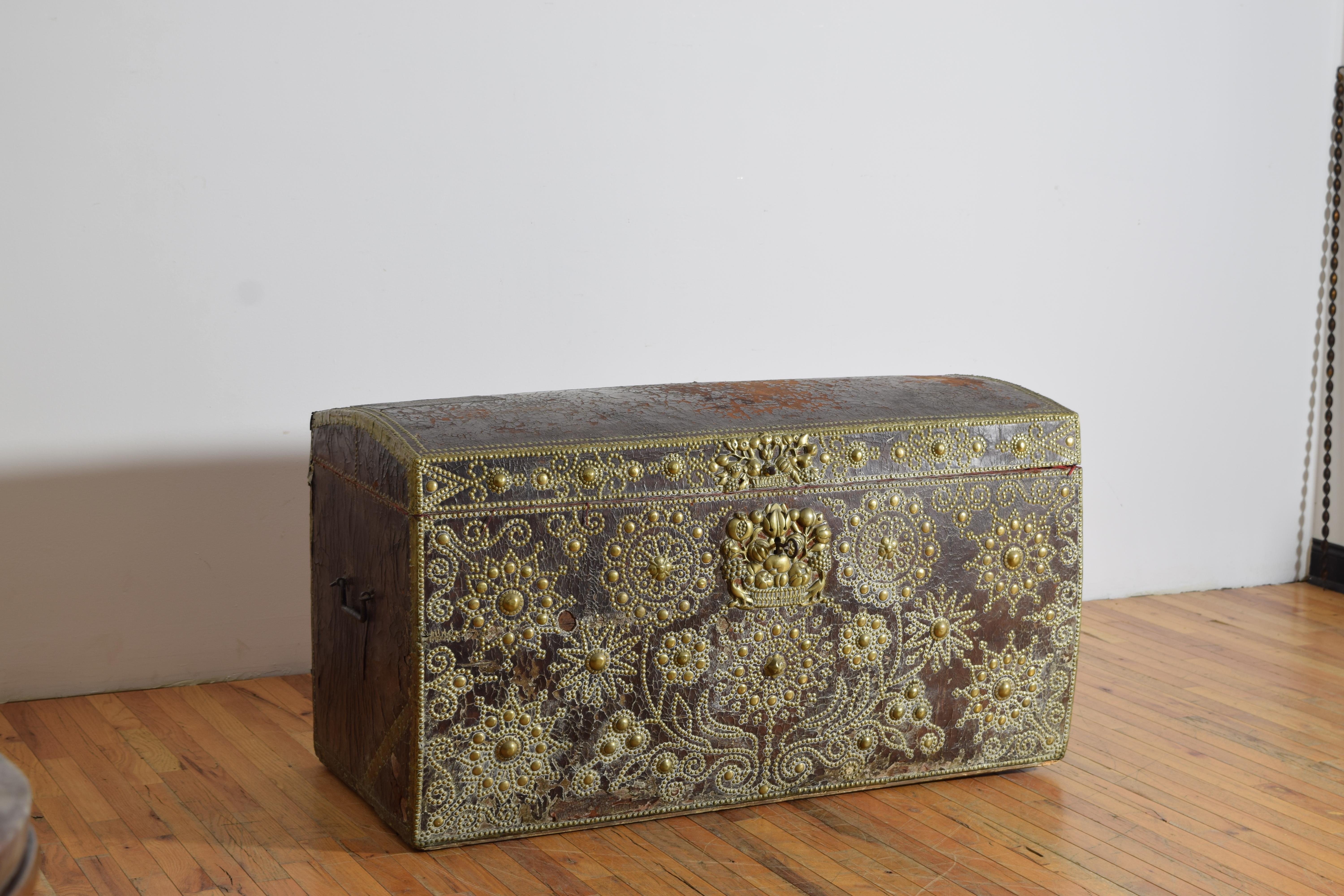 the trunk covered in leather and having a slightly domed top, the front elaborately decorated in brass nailheads and various decorative brass castings, with a brass nailhead trimmed top, the sides with original wrought iron carrying handles, the top