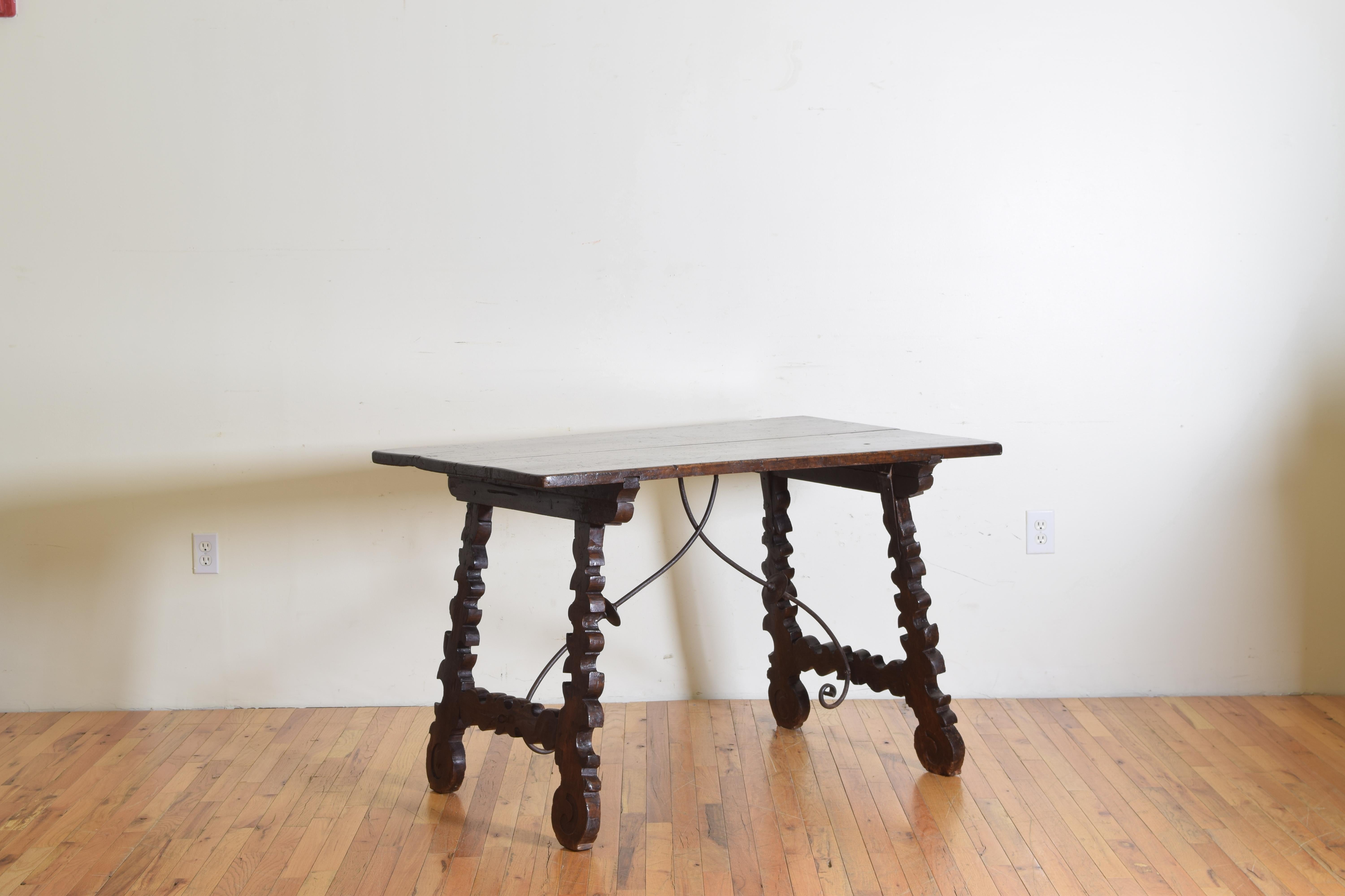 Having a rectangular two board top in walnut supported by hinged carved trestle-form legs ending in round feet, the iron double stretcher detaches from the legs in order to fold as these tables were originally made for portability and ease of