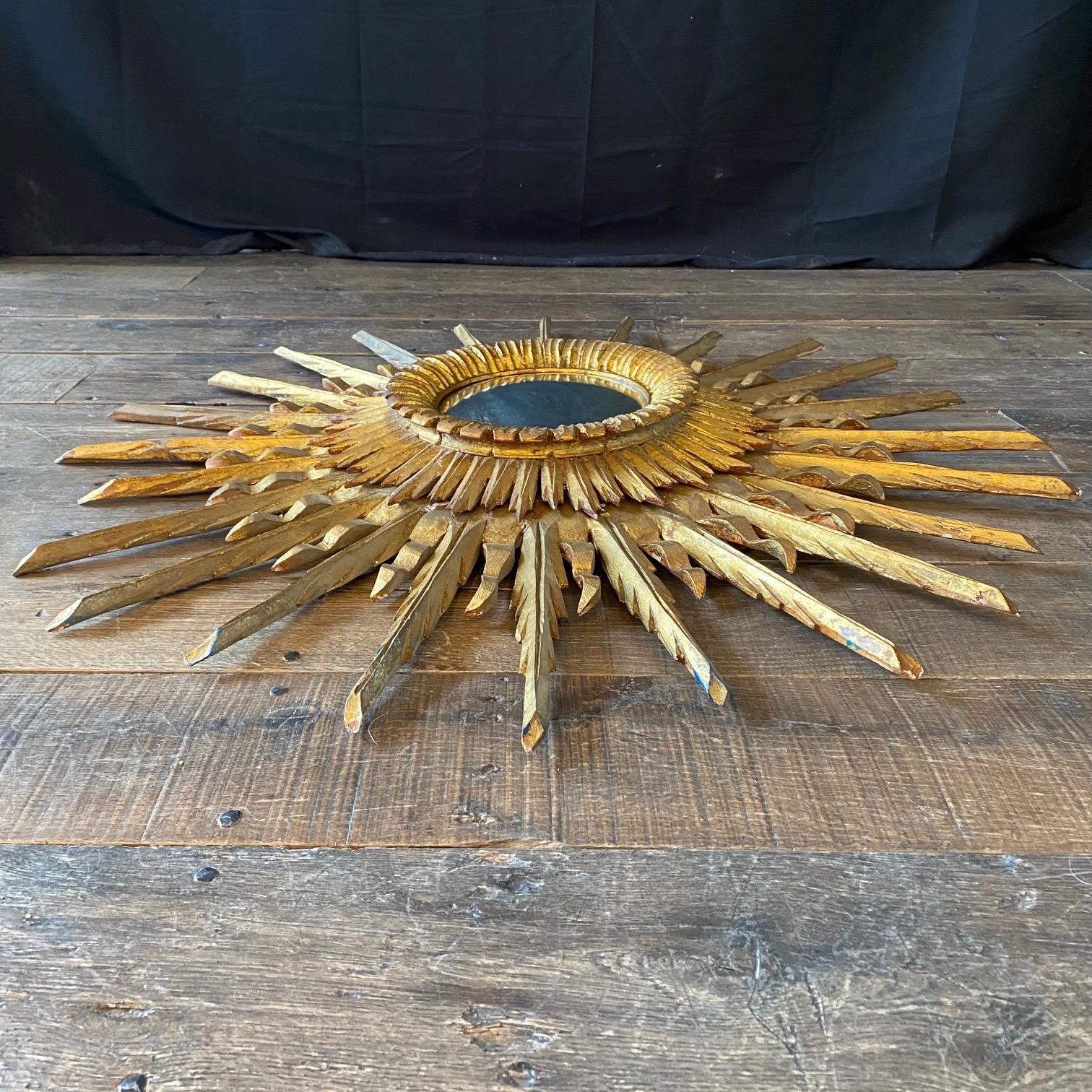 A very beautiful, layered, intricate and decorative large golden soleil sunburst or starburst giltwood convex mirror.  Handmade of carved stunningly gilt gold plated wood. One of our favorites. Whether hung in the entryway, living room, bedroom, or