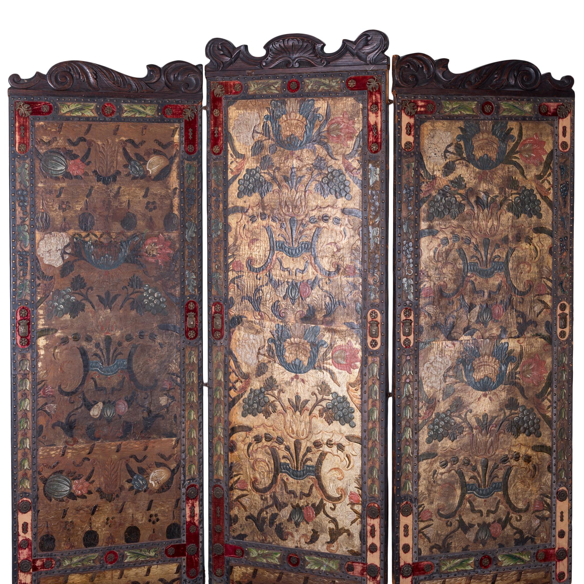 A Spanish leather screen from the 19th century. 

Tooled leather panels with polychrome flowers and grapes in a diamond stamped gilt field; mounted on carved chestnut frame with nailhead border ornamented with leaf and grape motif and inset red