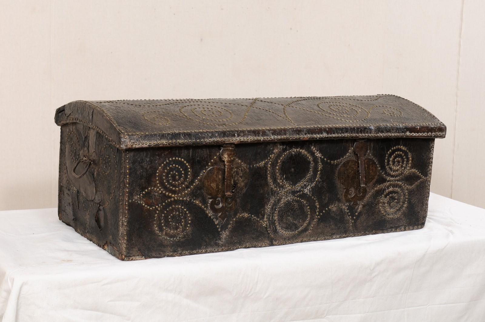 A Spanish coffer wrapped in leather and adorn with studs from the turn of the 18th and 19th century. This antique Spanish coffer, with it's rectangular-shaped body and slightly domed top, has been wrapped in leather and ornately adorn with nail-head