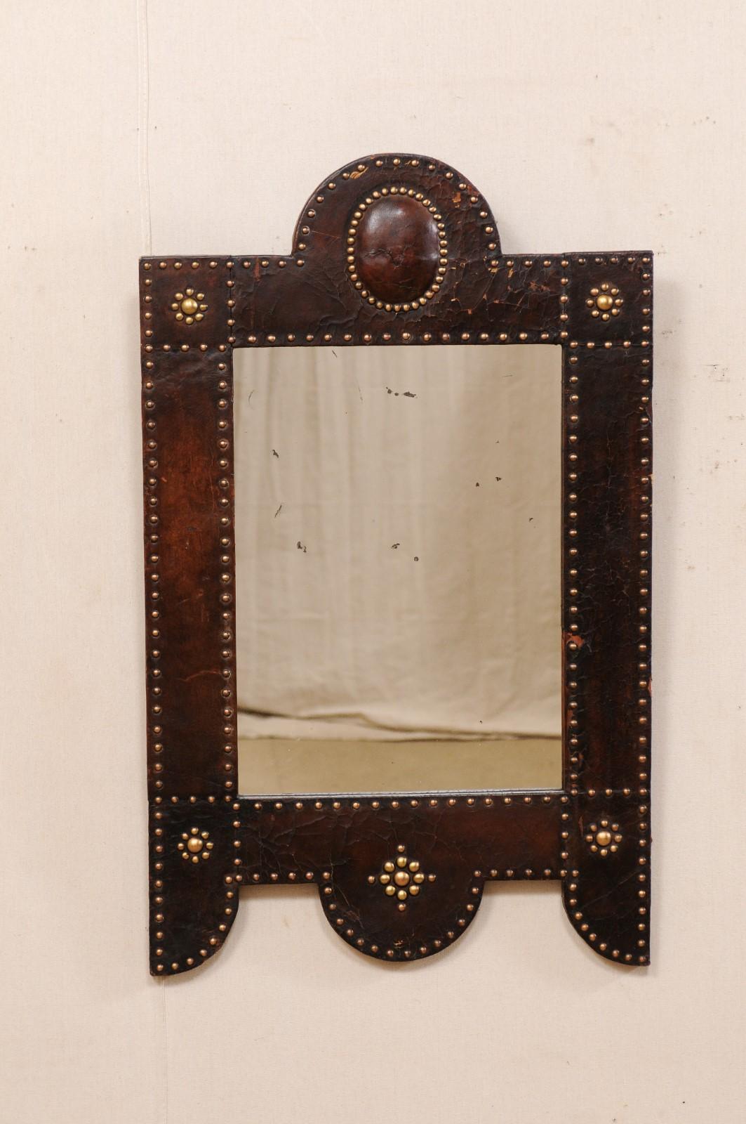 A Spanish leather wrapped mirror with brass nail-head accents from the mid to late 19th century. This antique mirror from Spain has a rectangular-shape with domed/arch at top center, which is repeated at bottom while being flanked by elongated sides
