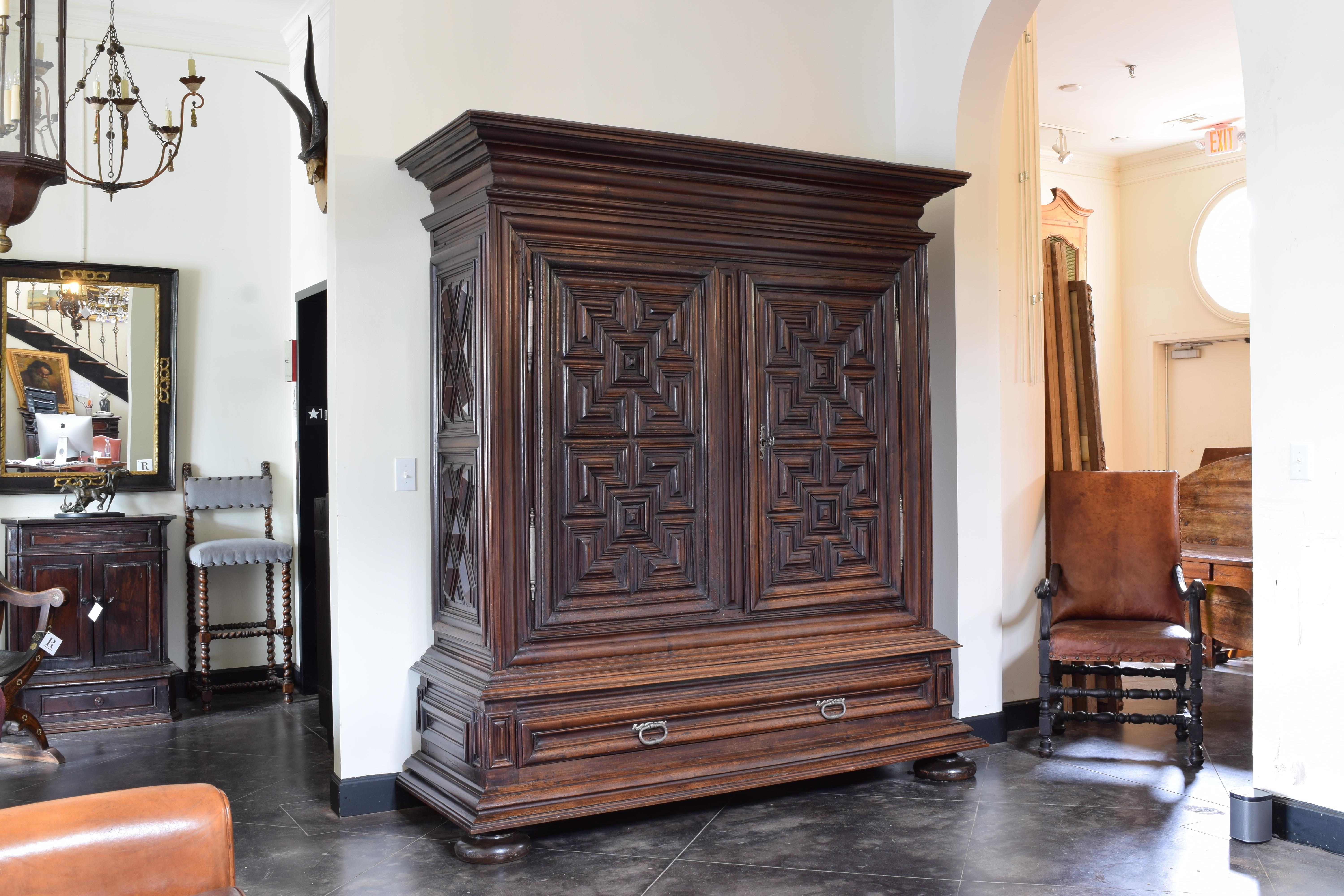 This beautiful bestia features a wide and deep stepped cornice atop a large case with geometric carved paneled sides and two geometric carved paneled doors, all the carvings deep and expertly performed, the case atop a graduated plinth-form bottom