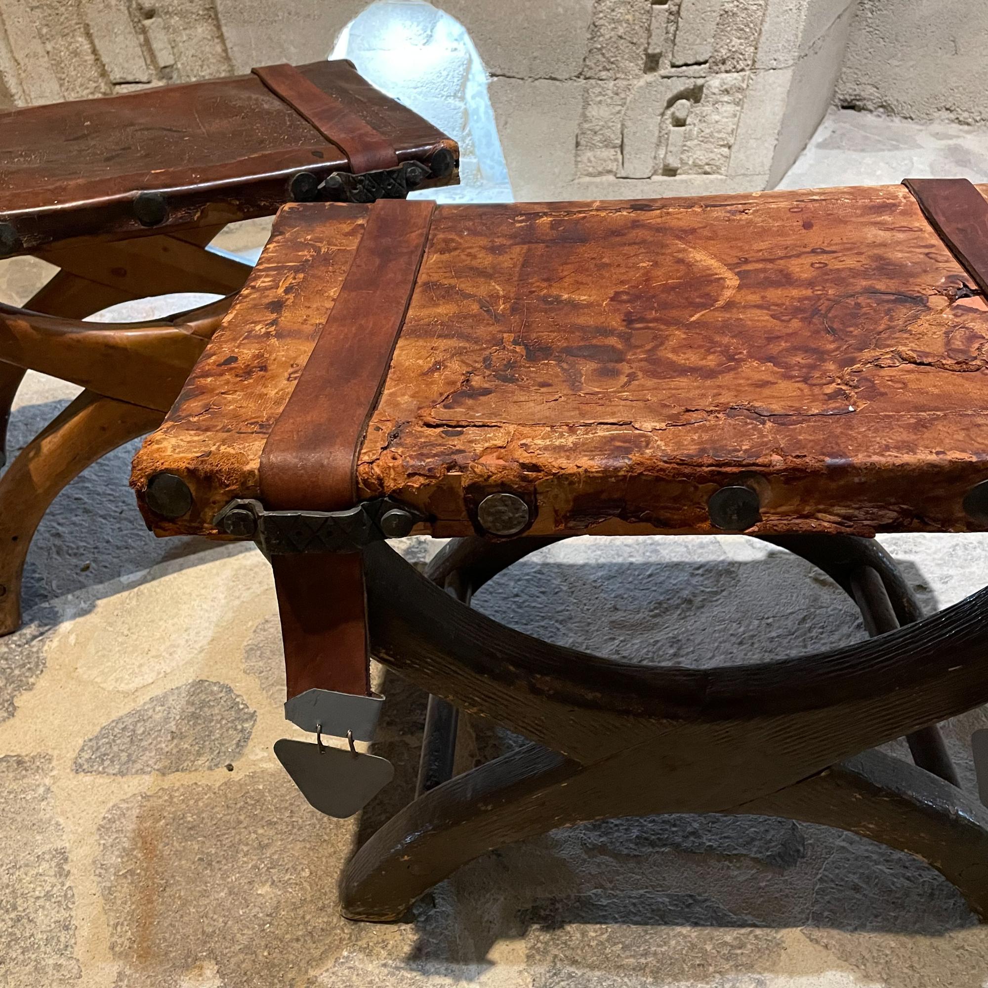 1940s Spanish colonial curule stools made in Mexico. Set of two.
Latin American rustic leather seat and strap. Fabulous medallions.
In the style of Clara Porset & Luis Barragan. 
Similar to Miguelito Butaque.
Unmarked. 
Features weathered patina,