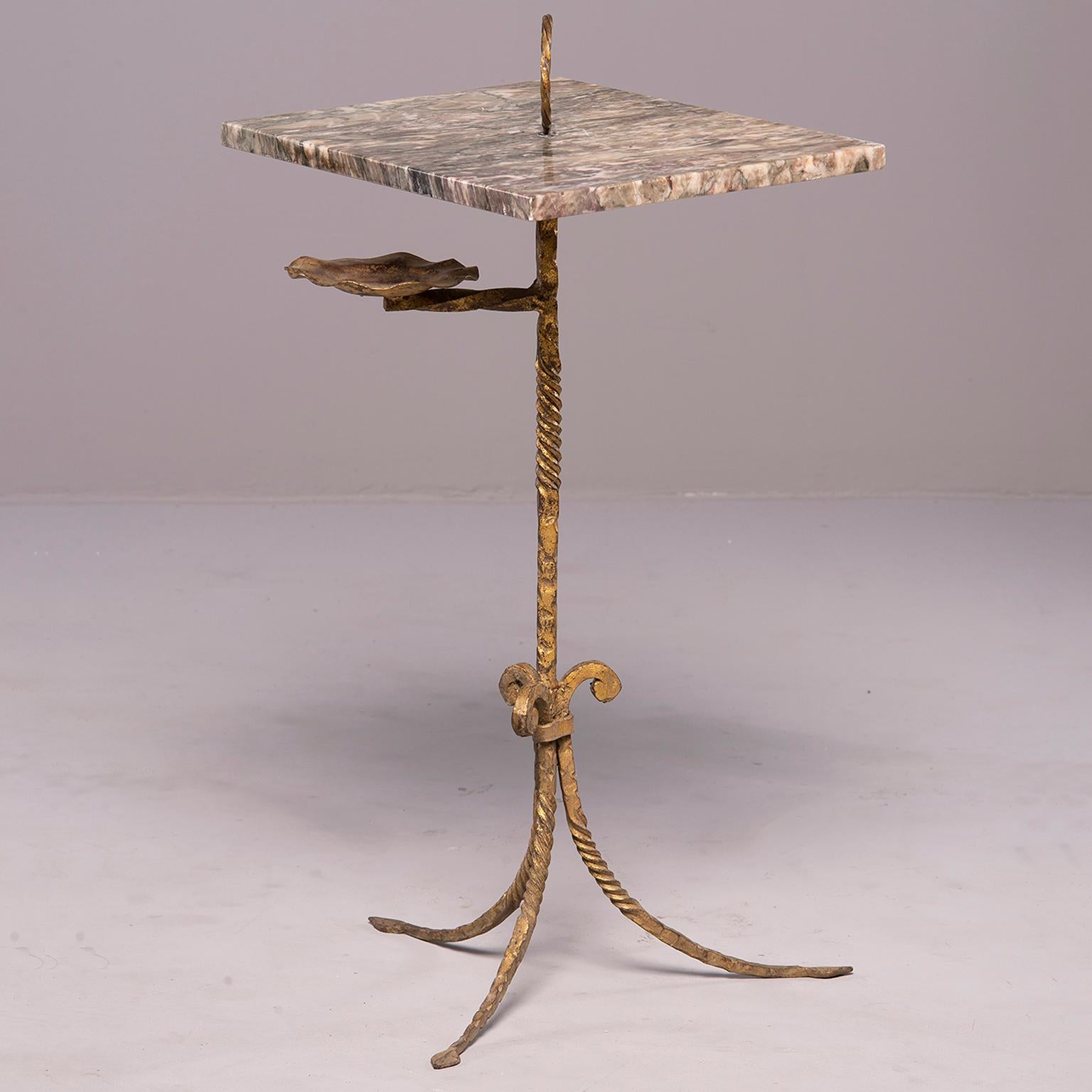 Spanish side table has an iron base with tripod feet, twisted surface details and gilded finish, circa 1930s. Rectangular marble top in gray tones with ring shaped topper and gilt metal ashtray holder below table. Unknown maker. Very good vintage